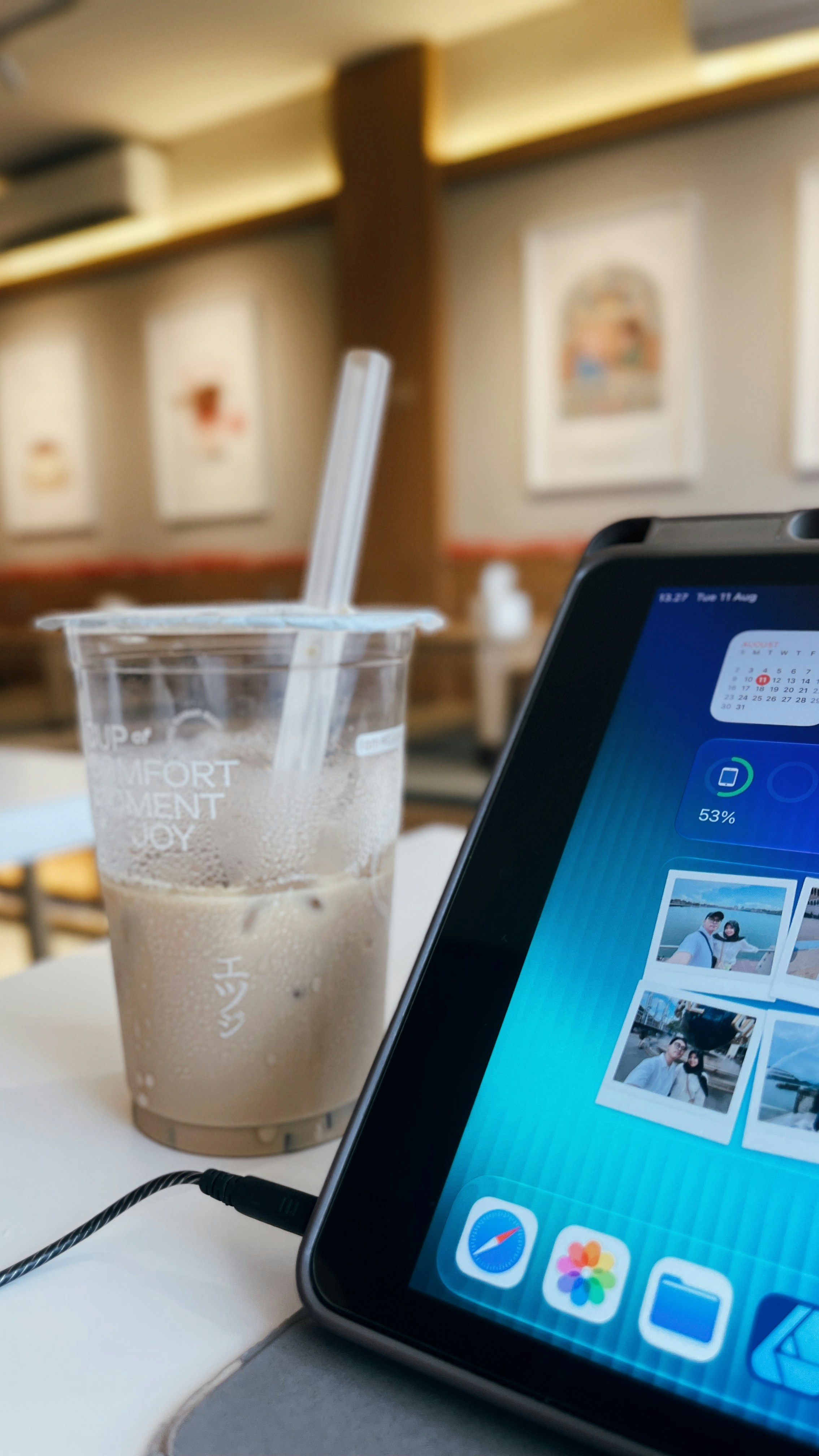 An iced coffee in a plastic cup beside a tablet on a table