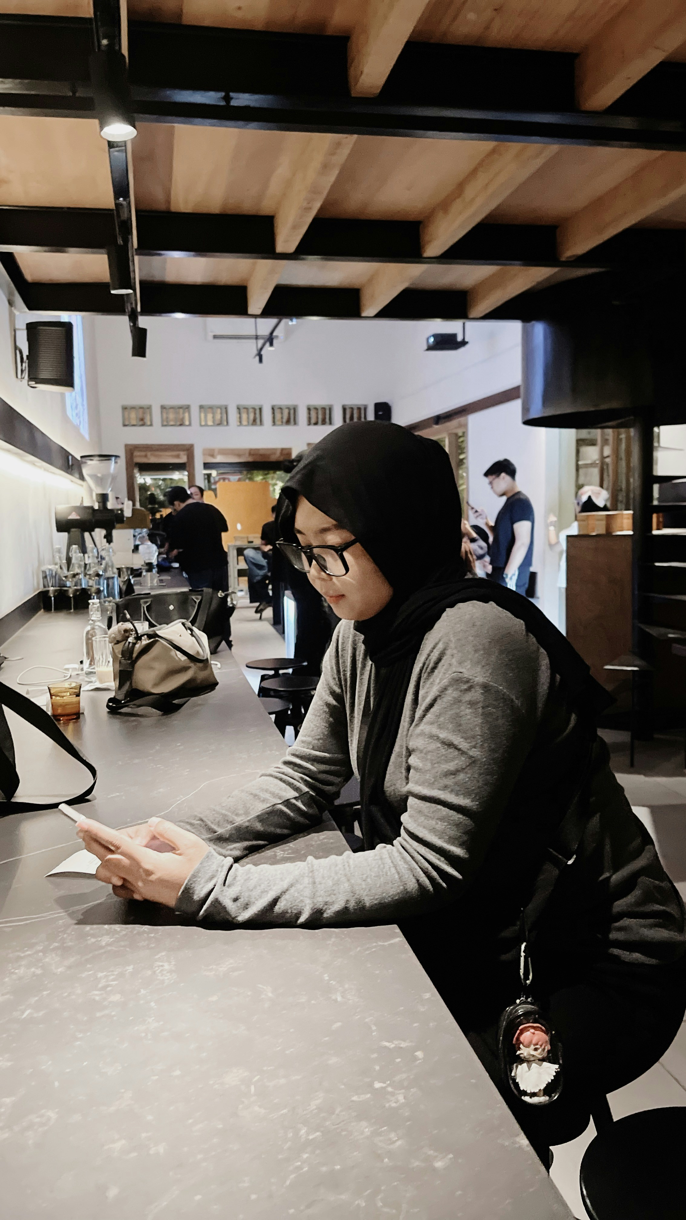 A woman in a black hijab and glasses using a smartphone at a cafe counter