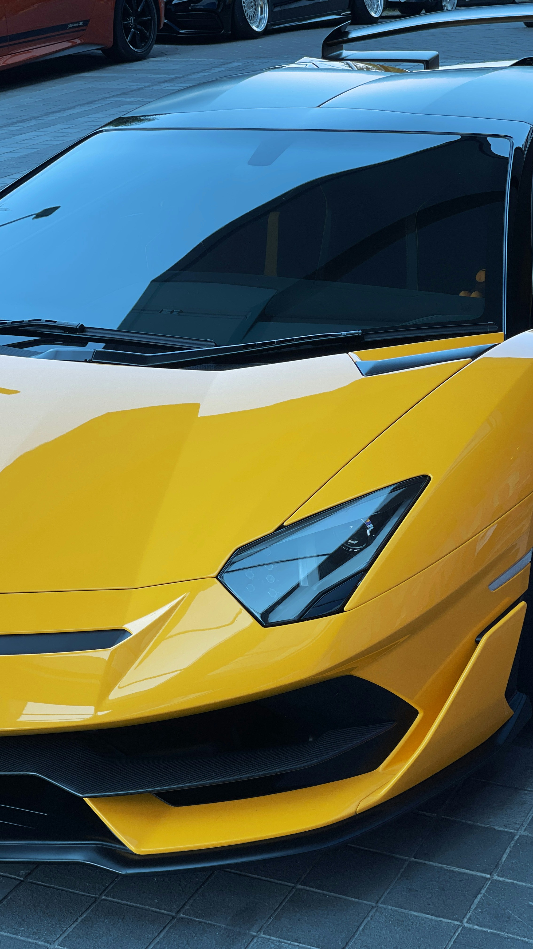 The front hood and headlight of a yellow sports car on pavement