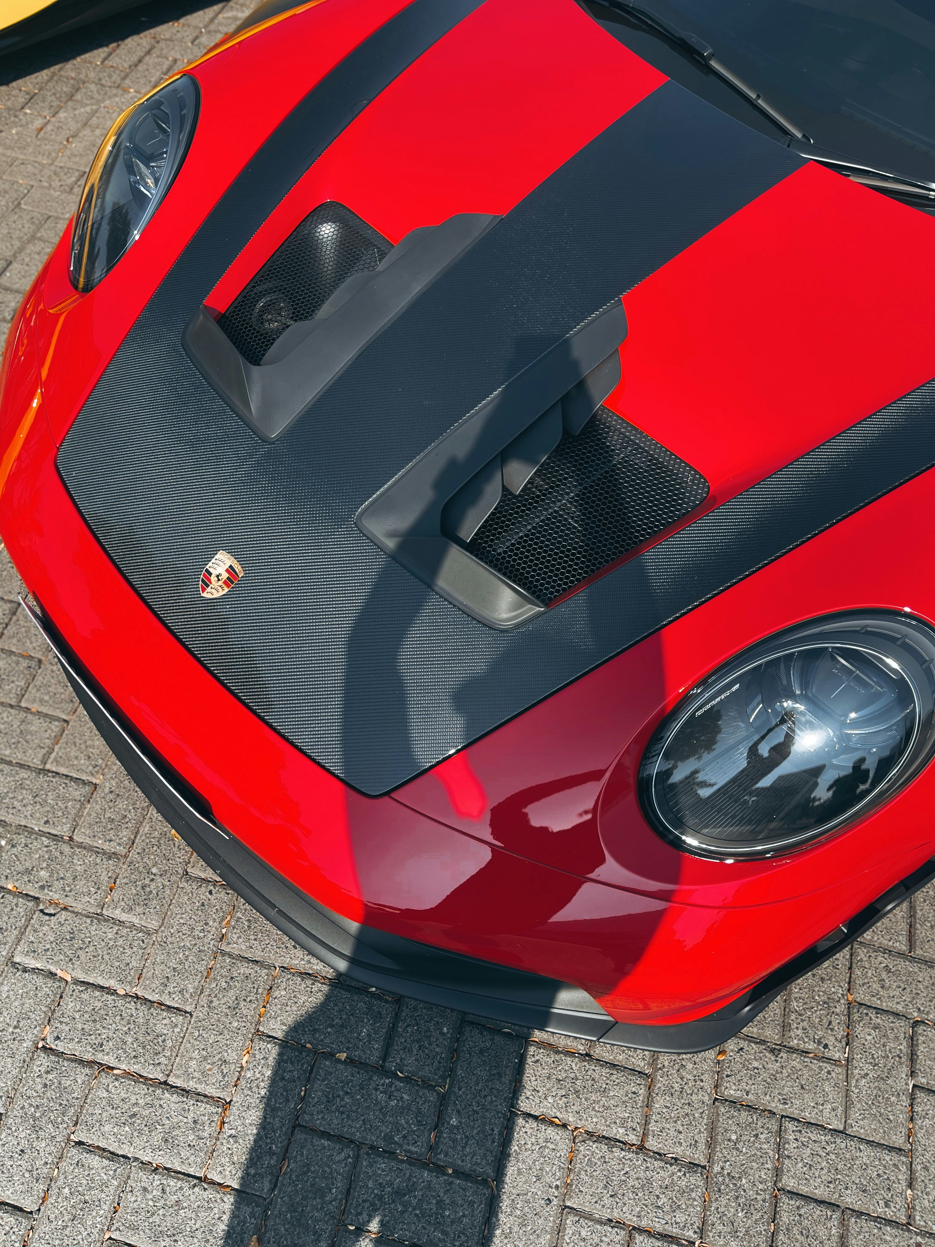 A red Porsche sports car with a black carbon fiber hood on brick pavement