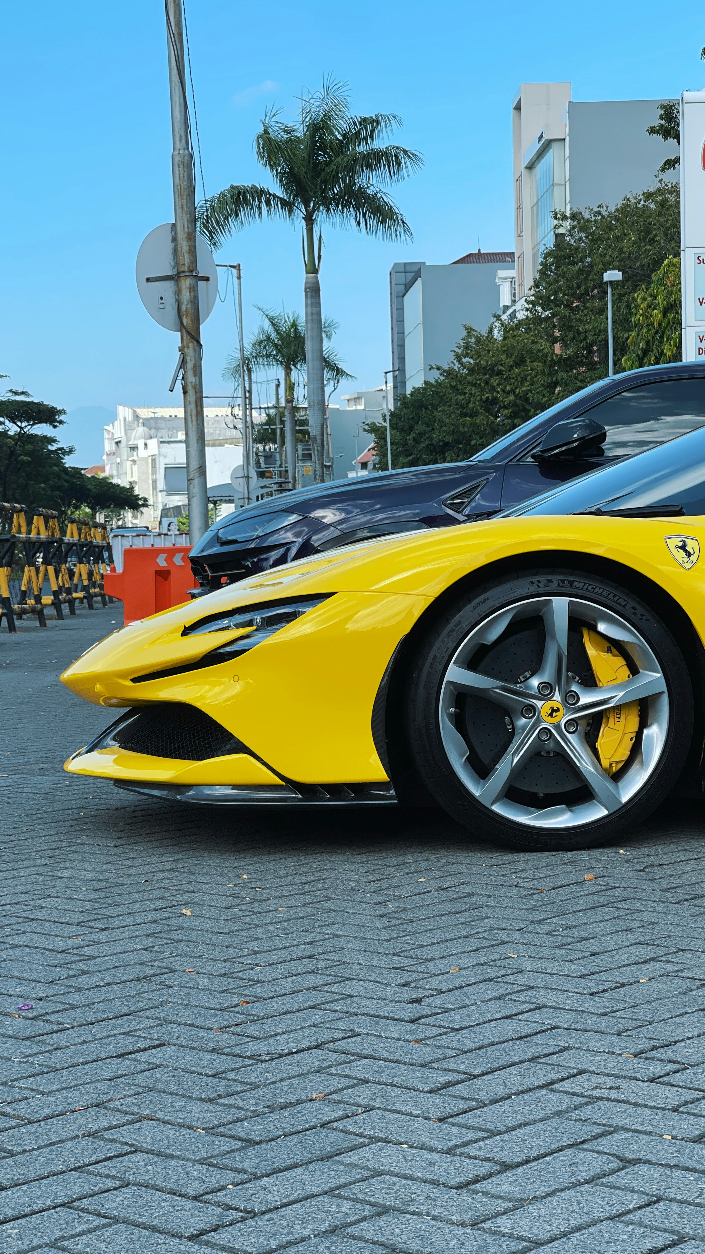 A yellow sports car parked on a grey paved street with palm trees
