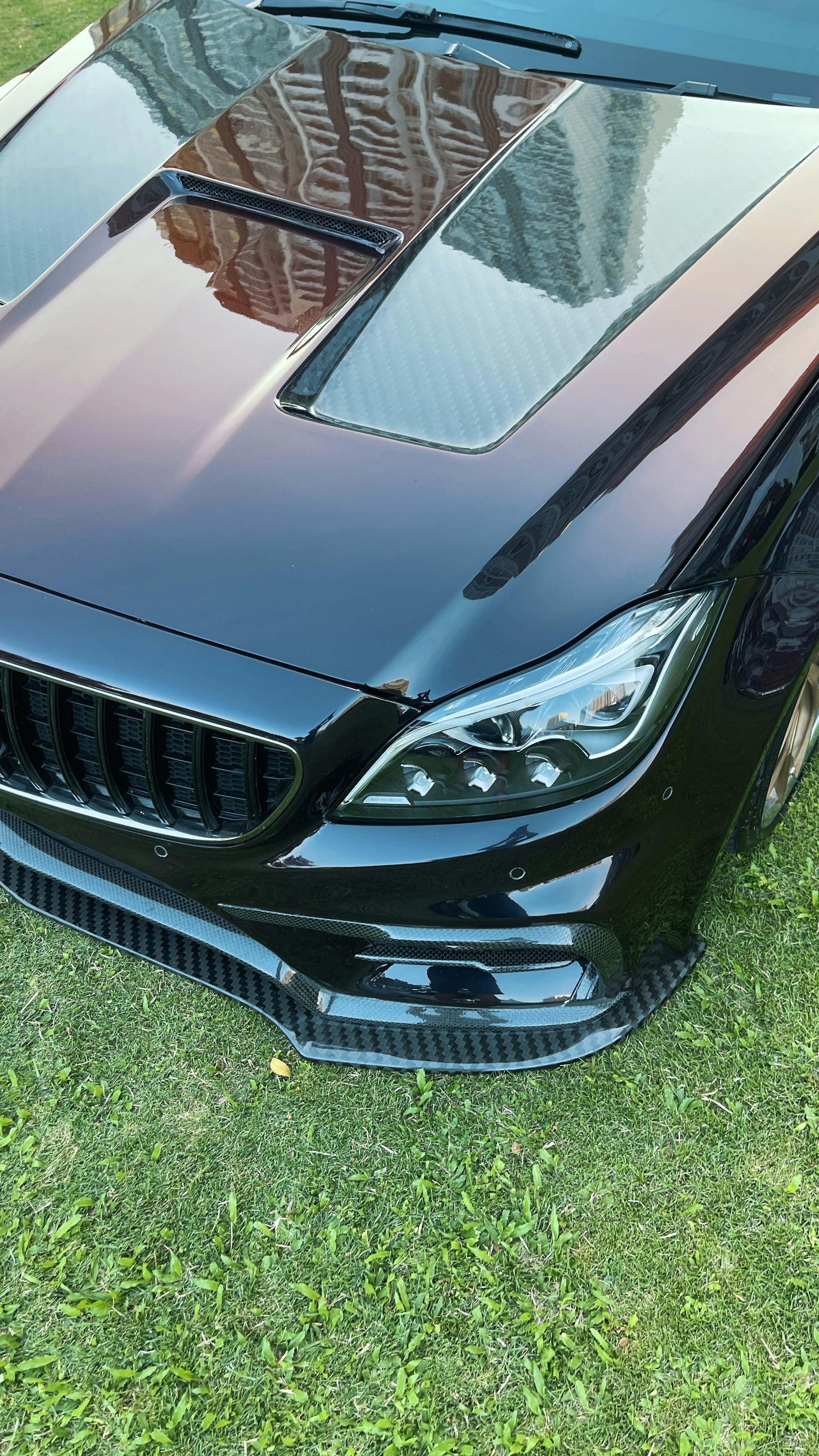 A black car with a carbon fiber hood and front splitter on green grass