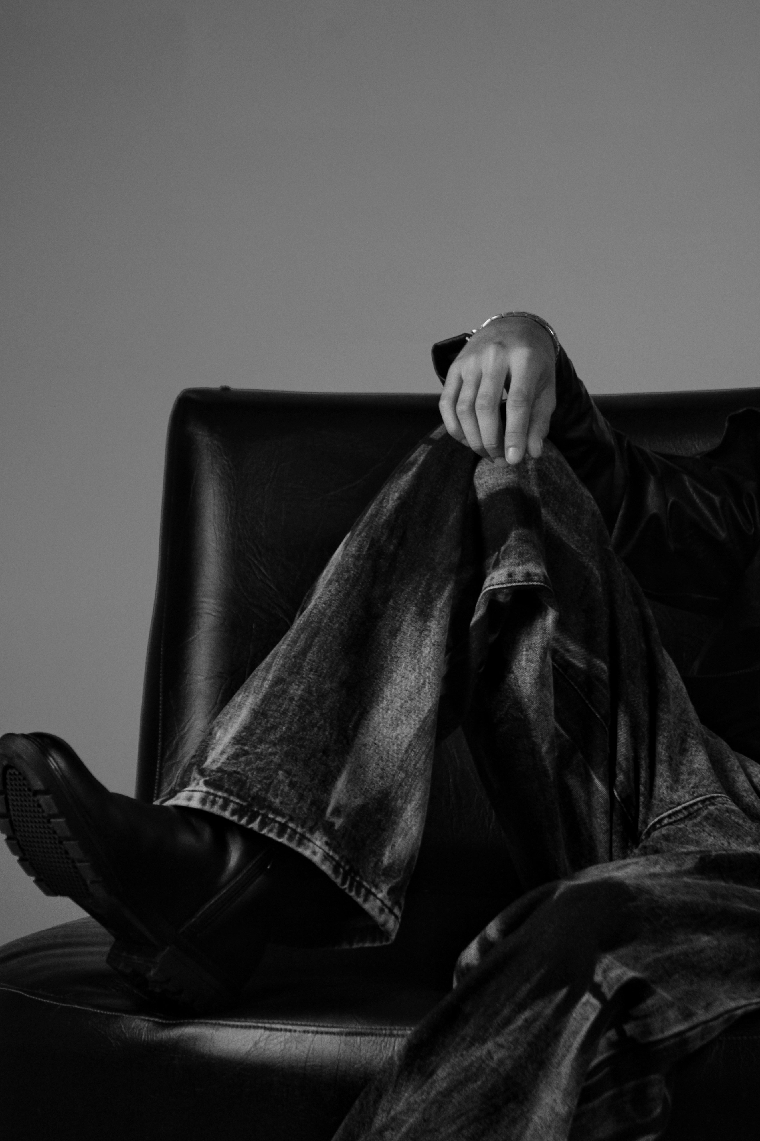A person in acid-wash jeans and black boots sitting on a leather chair