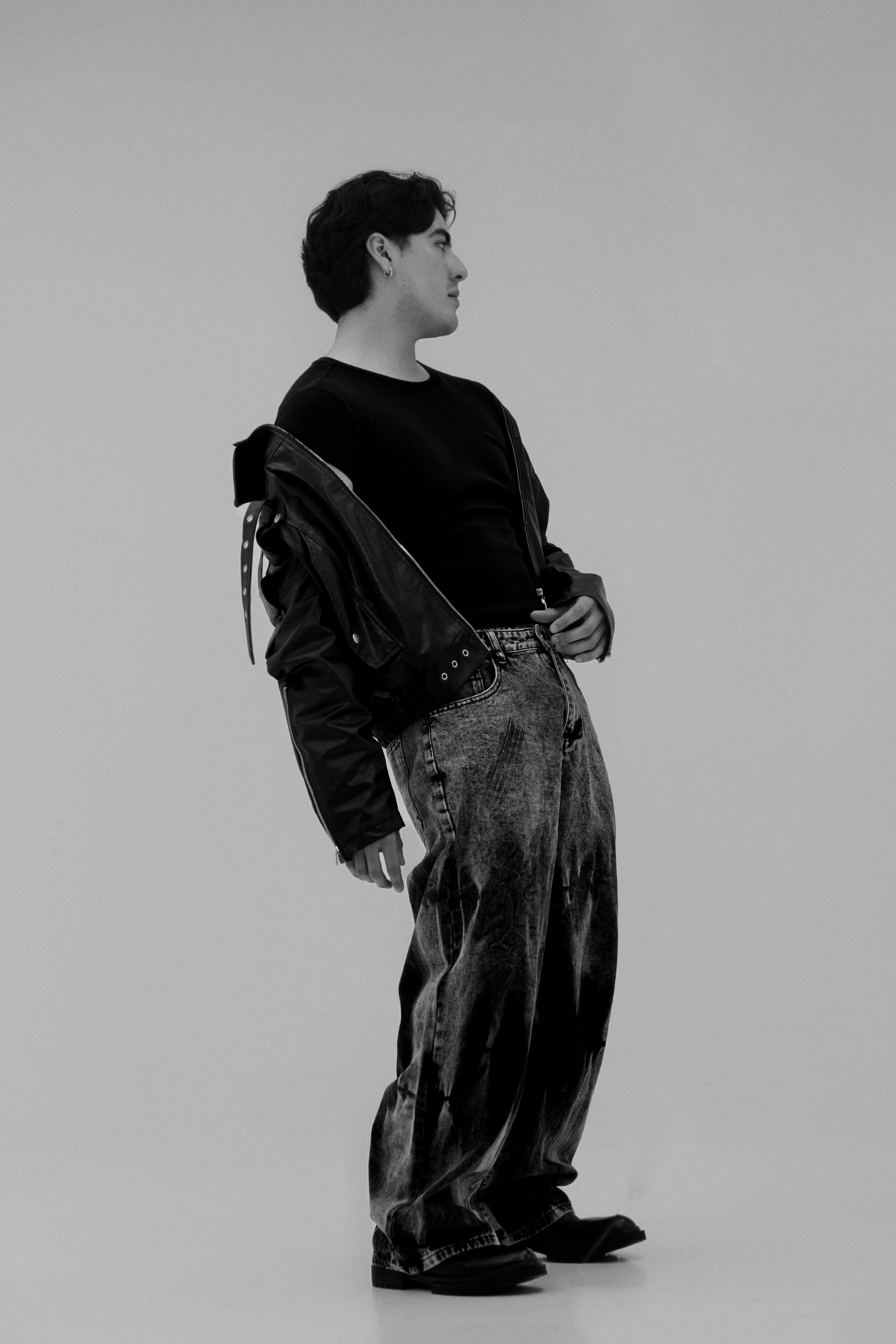 A person in a black t-shirt, leather jacket, and acid-wash jeans