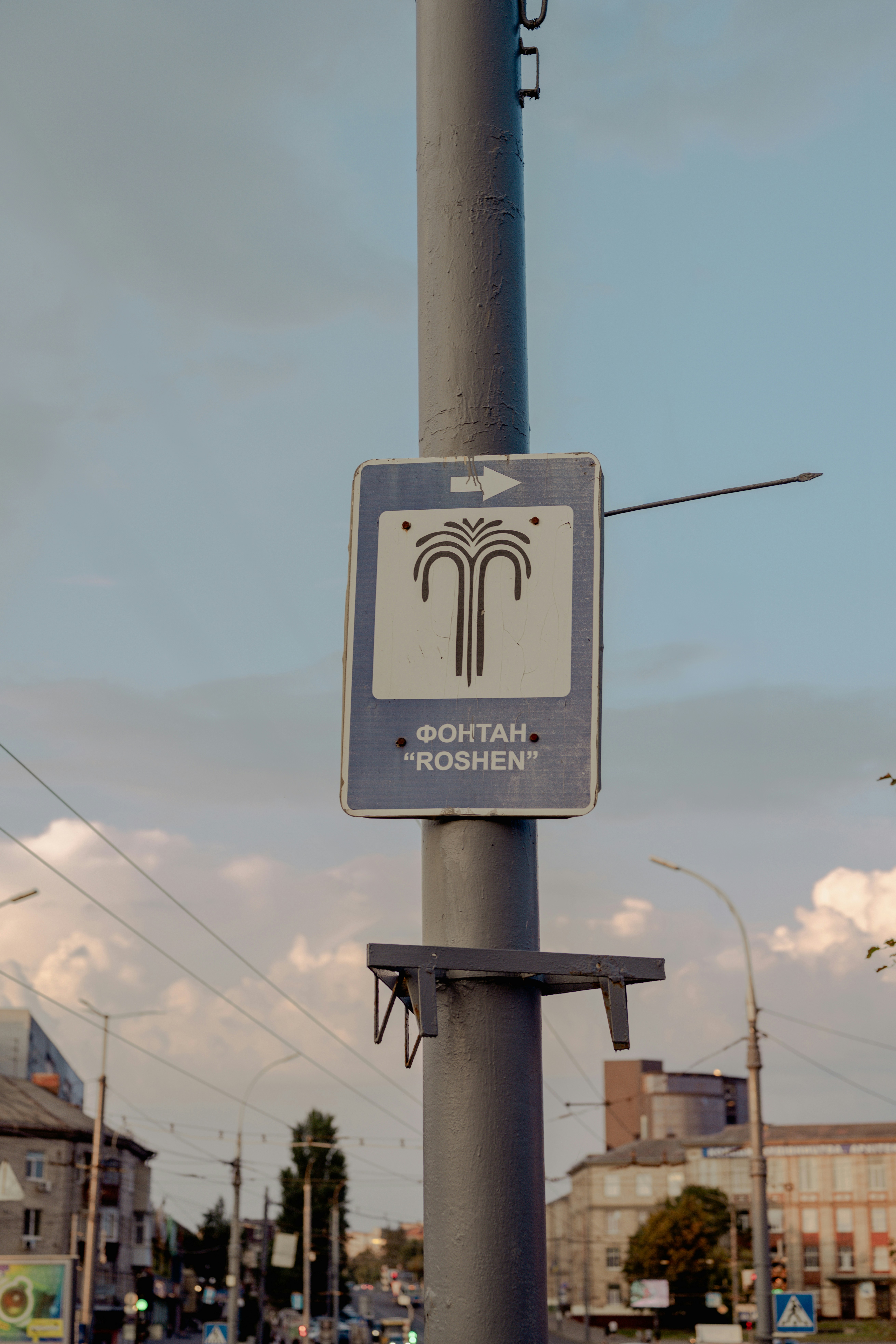 A blue directional sign for Roshen fountain on a metal pole in a city
