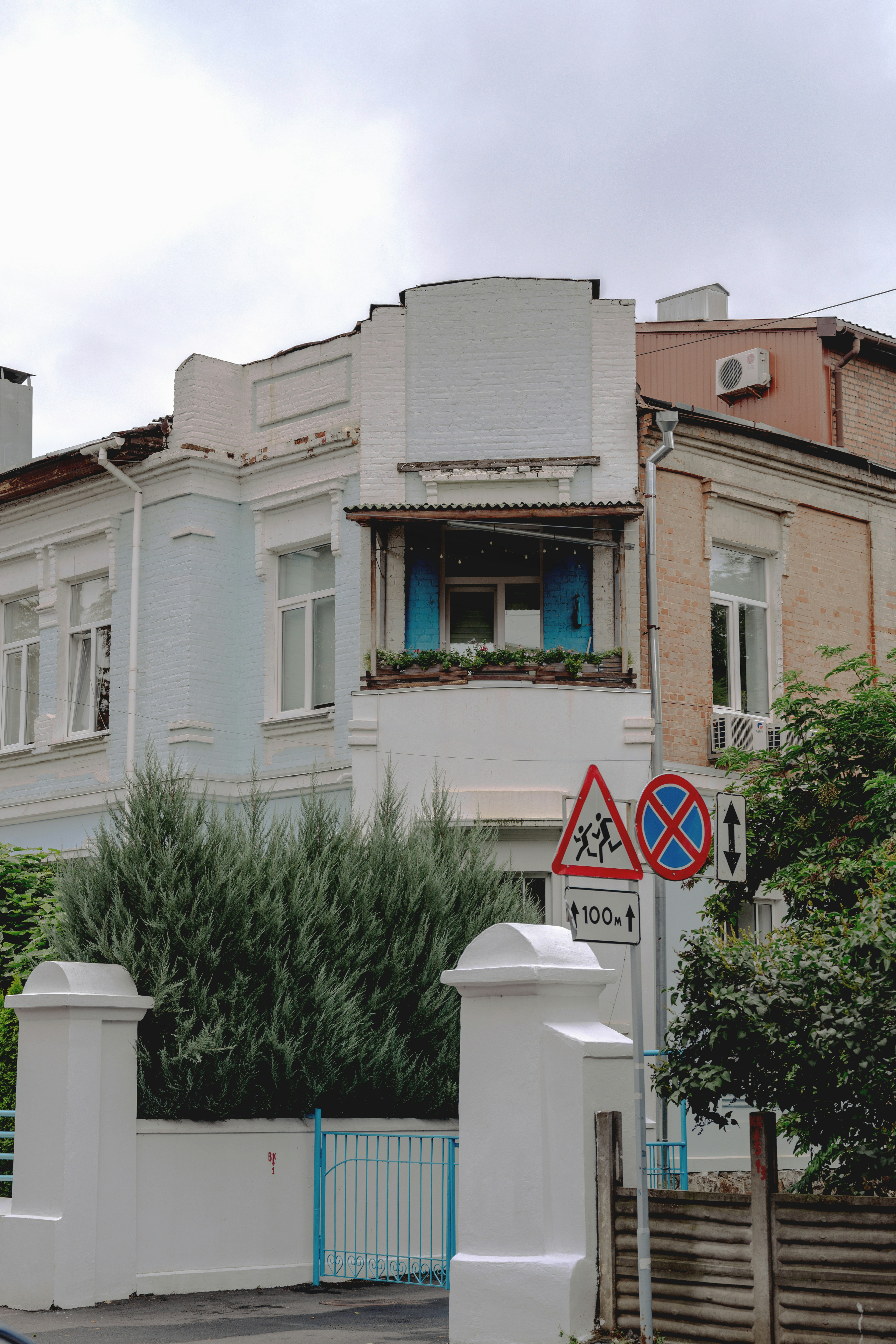 A light blue building with a balcony and traffic signs on a street