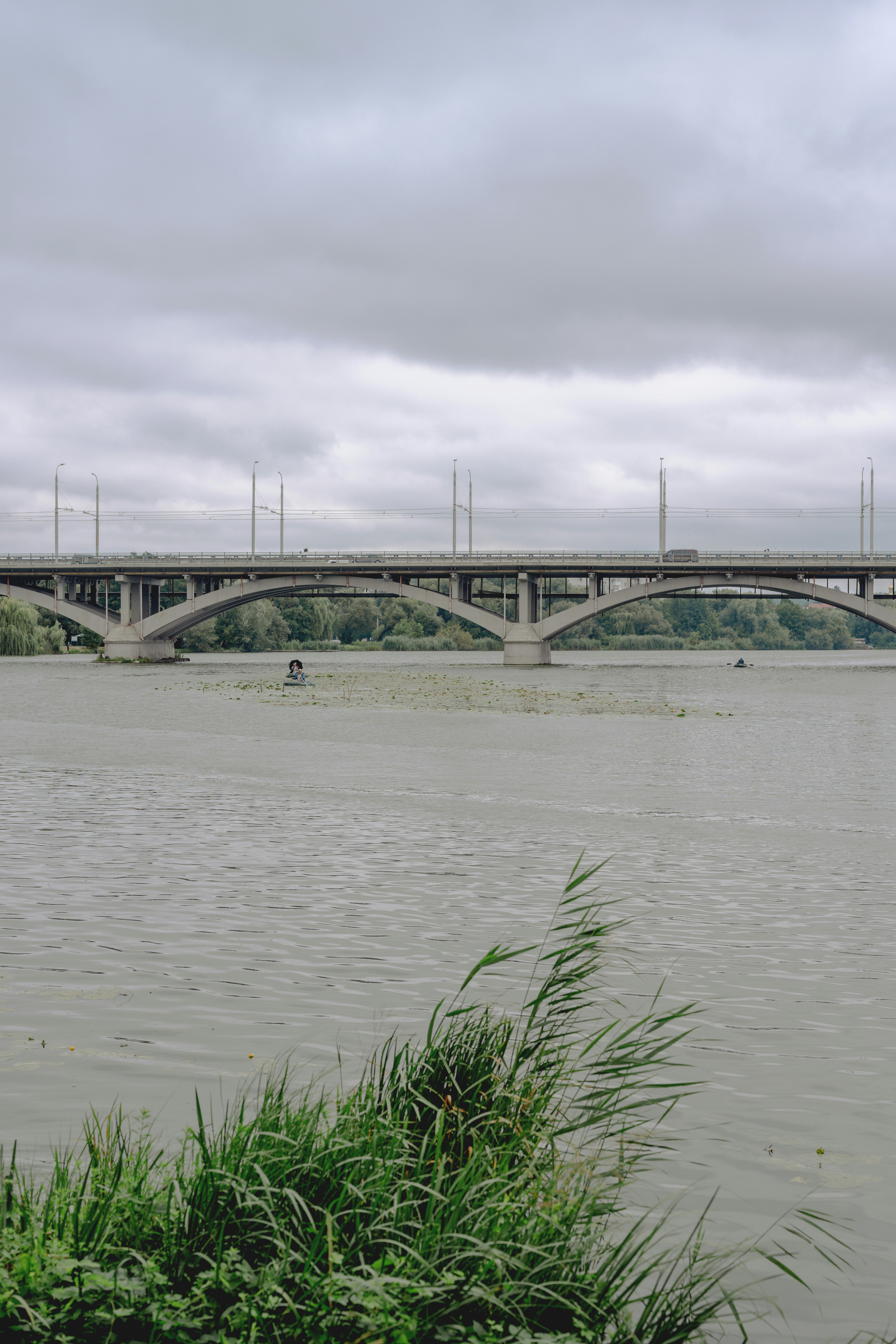 A concrete arch bridge spanning a wide river under a cloudy grey sky