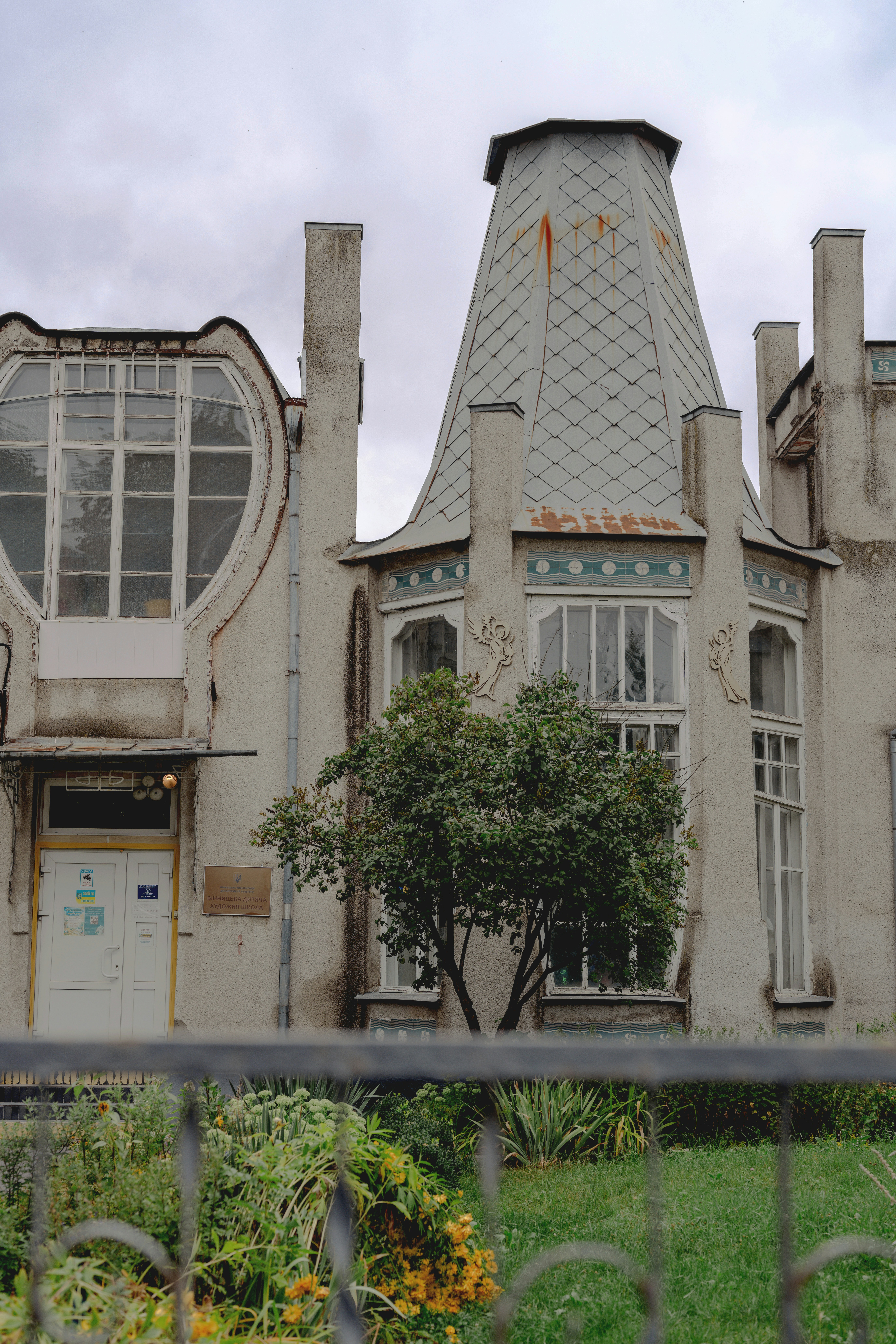 An art nouveau building with a tall conical roof and a tree in front
