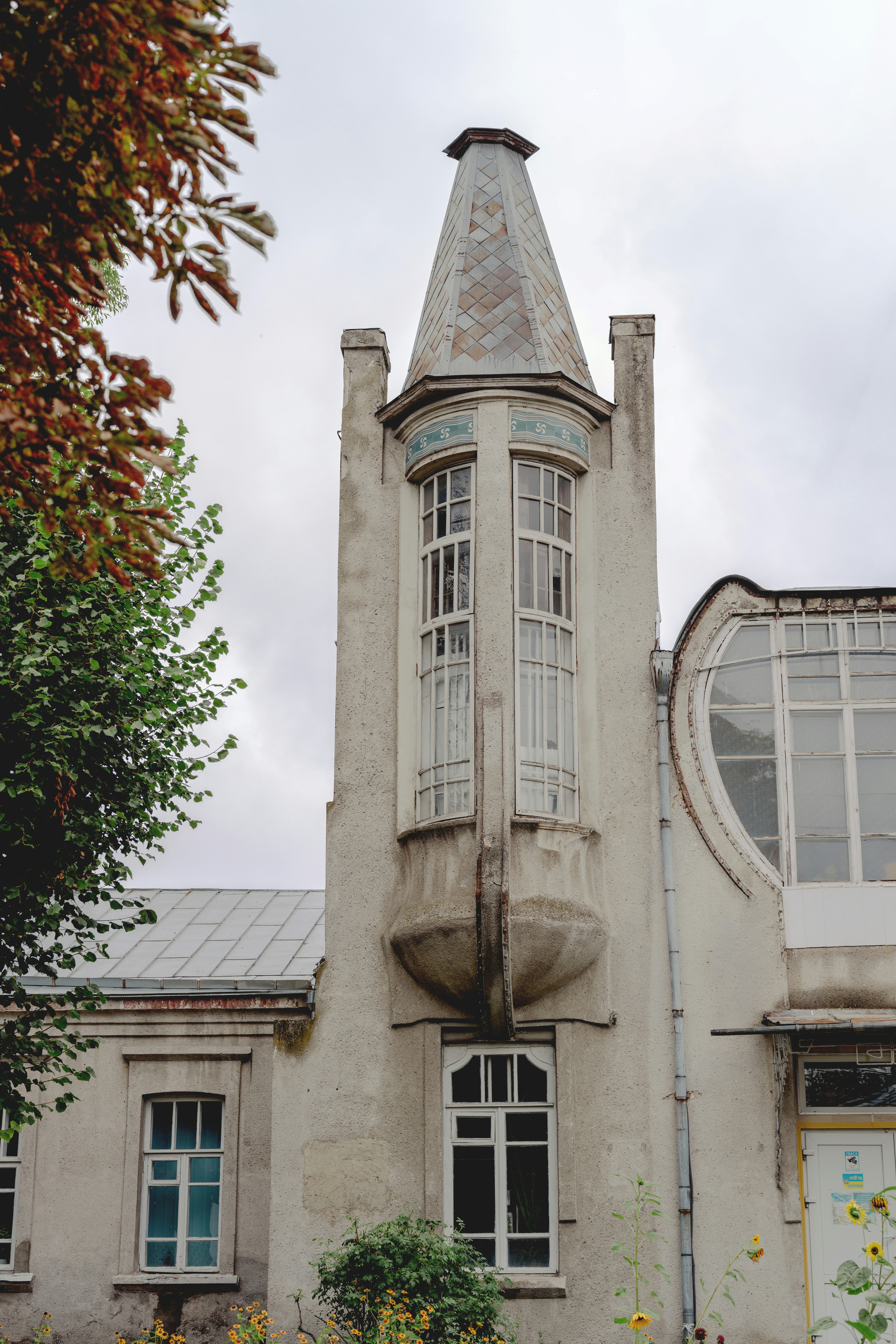 A tall turret with a tiled roof on a light-colored building with arched windows