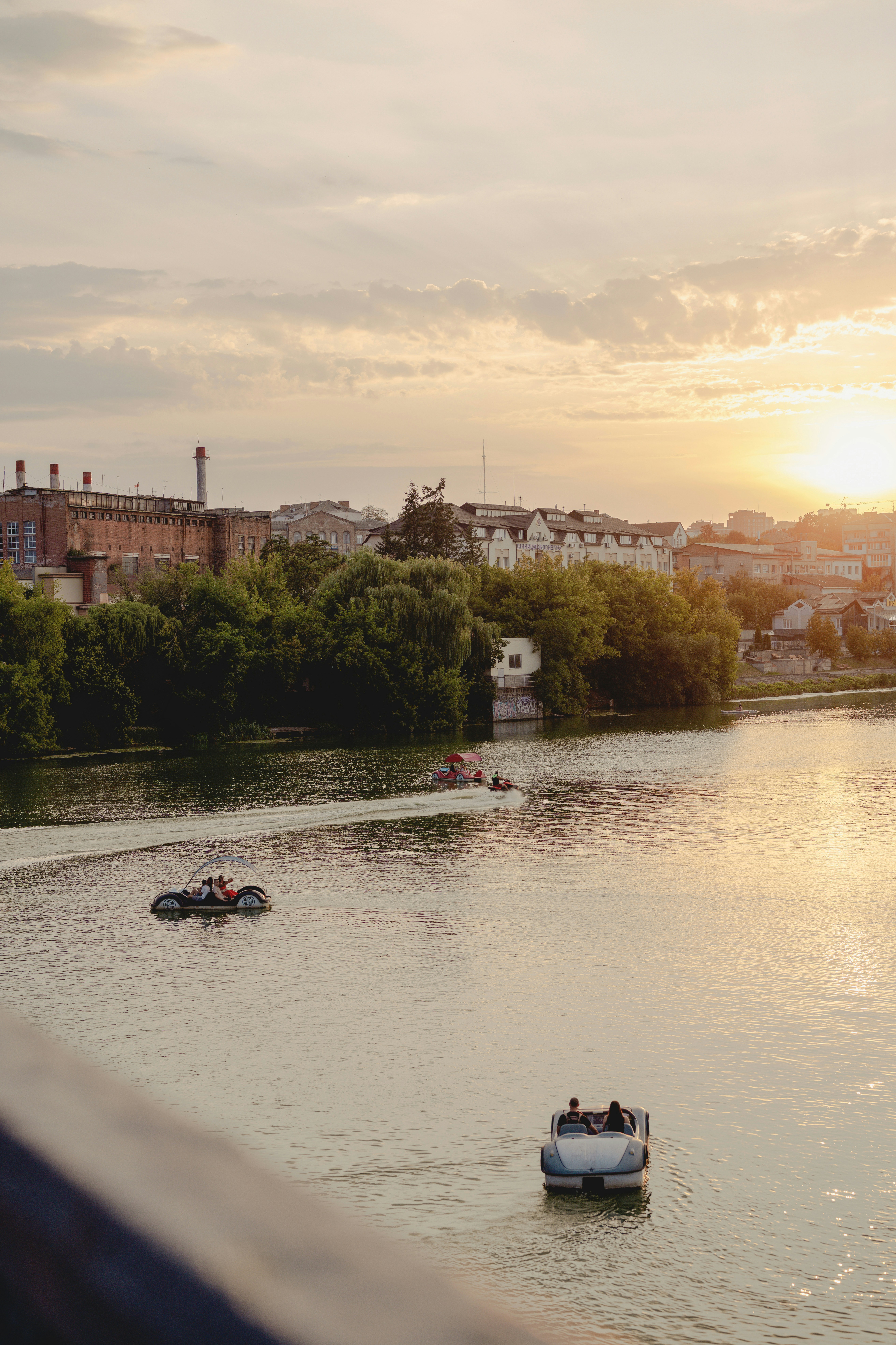 People in pedal boats on a river near a city during golden hour