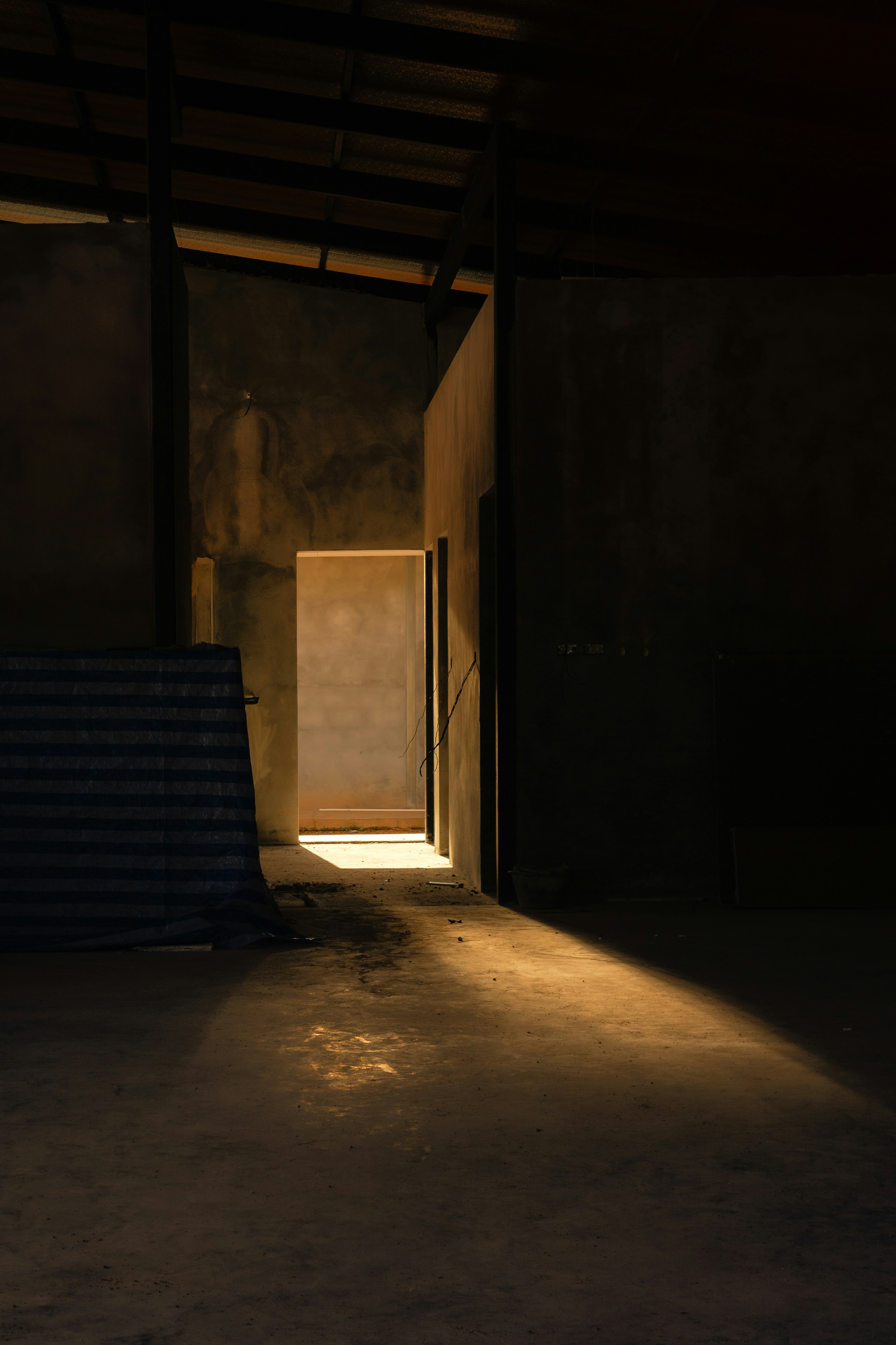A doorway casting a long beam of warm light across a dark concrete floor