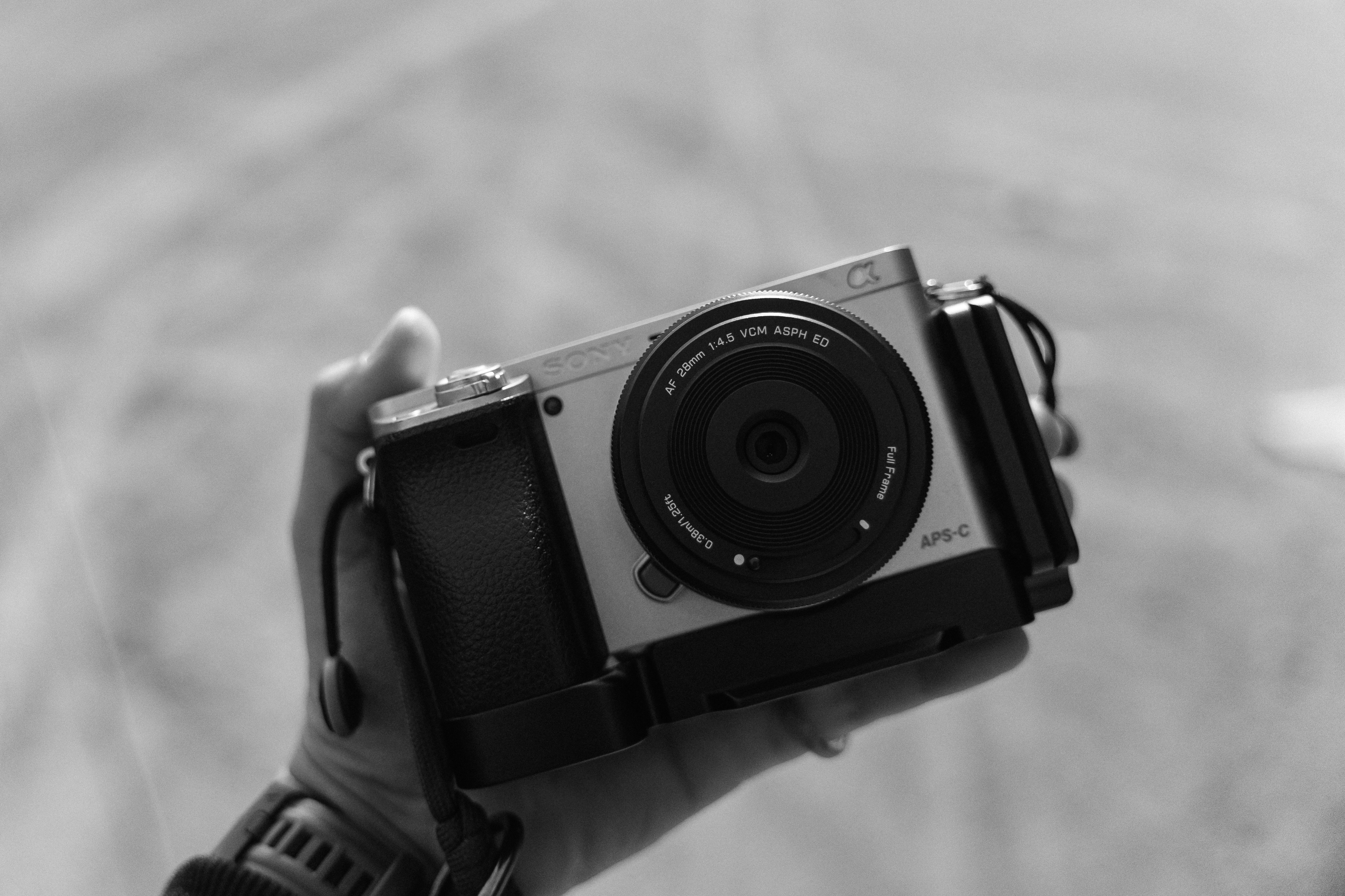 A hand holding a silver mirrorless camera with a black lens