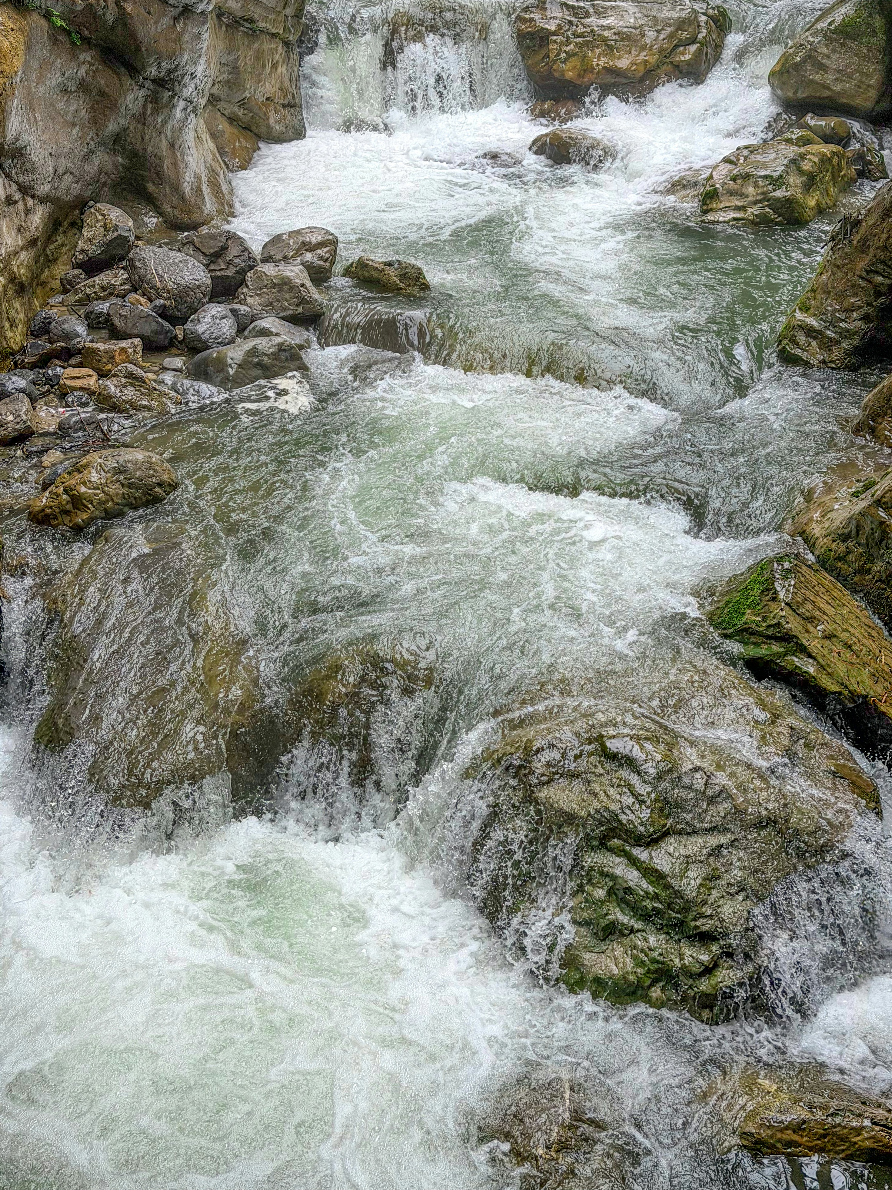 A rushing mountain stream flowing over mossy rocks and boulders