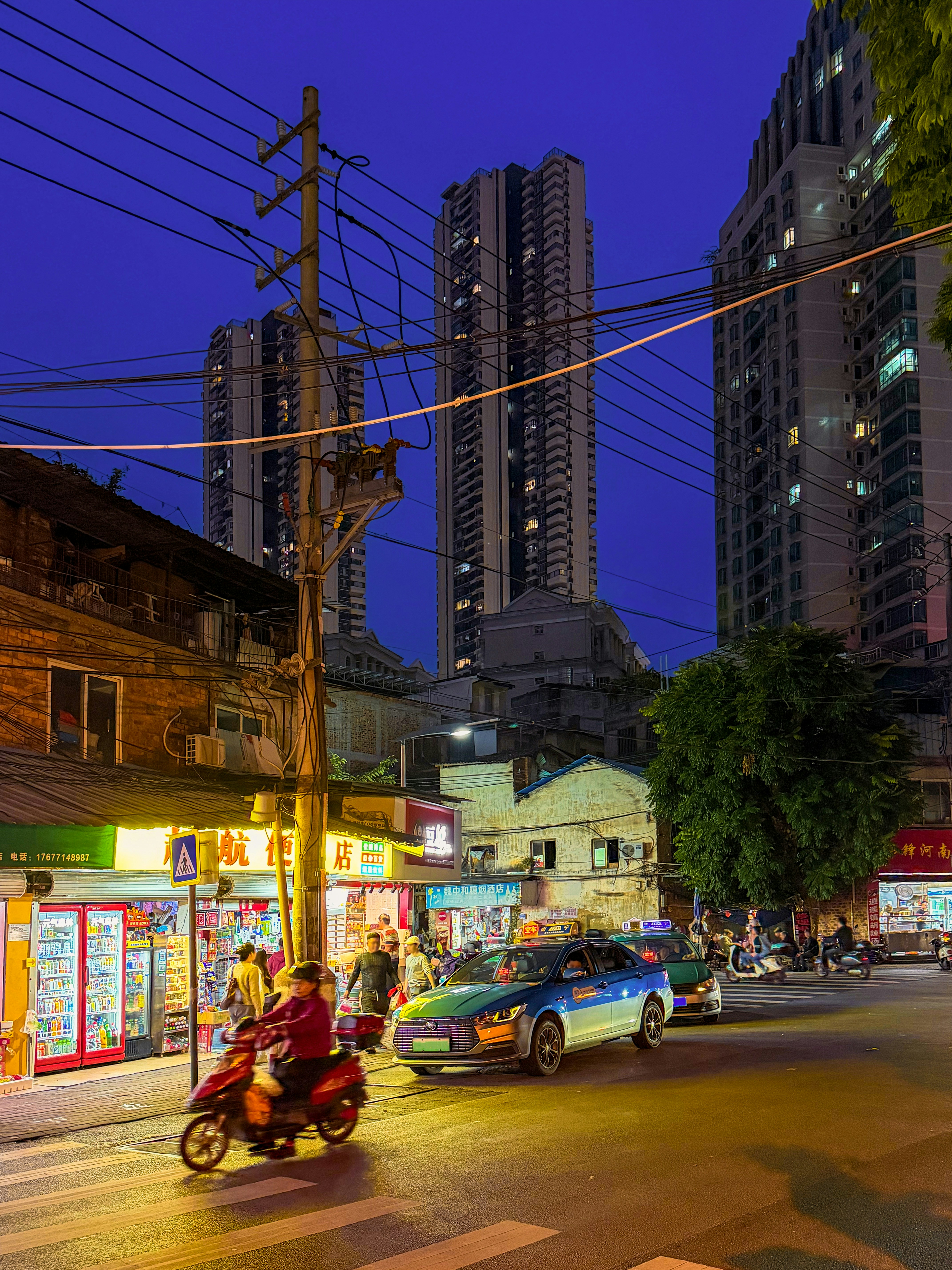 A person riding a red scooter past a brightly lit shop at night