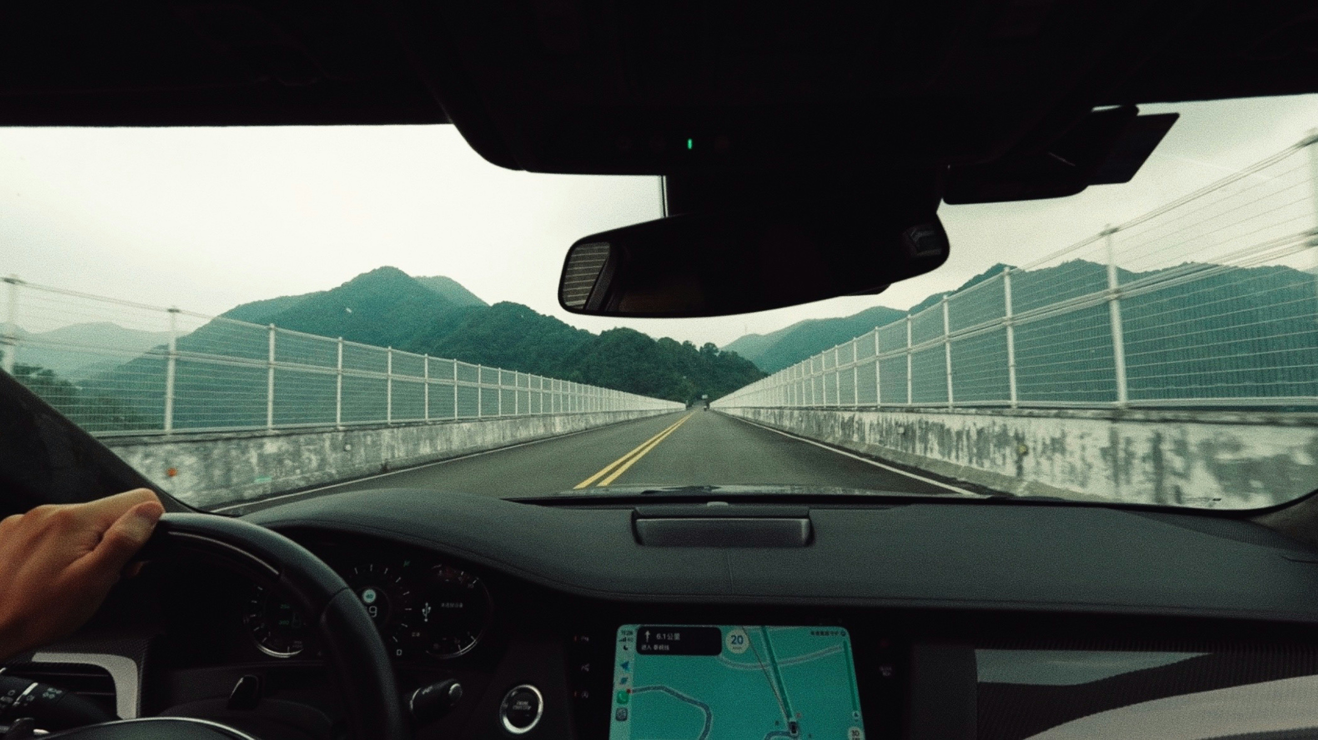 A person driving a car on a highway between green mountains