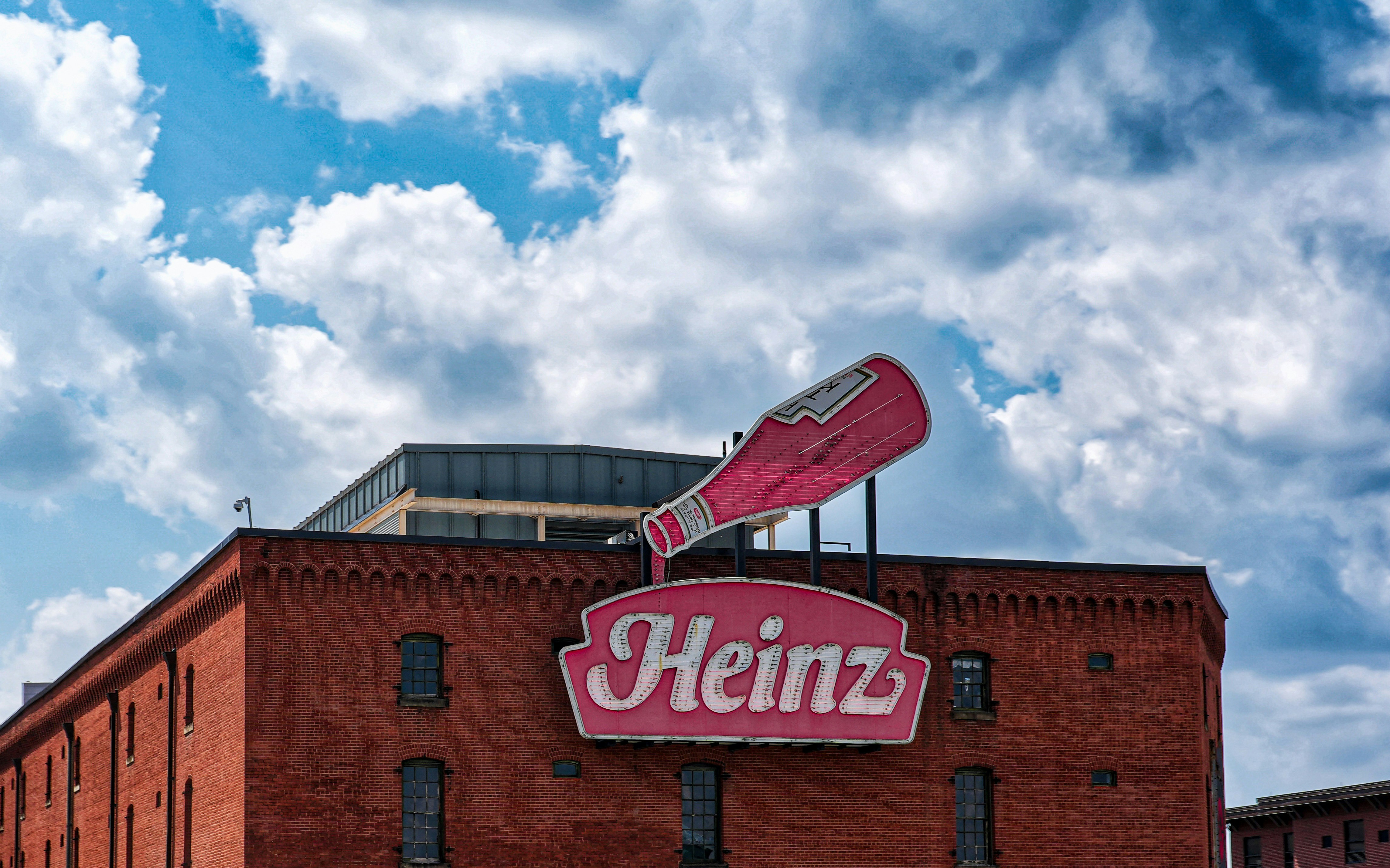 Un grand bâtiment en briques rouges avec une enseigne au néon Heinz sur le toit