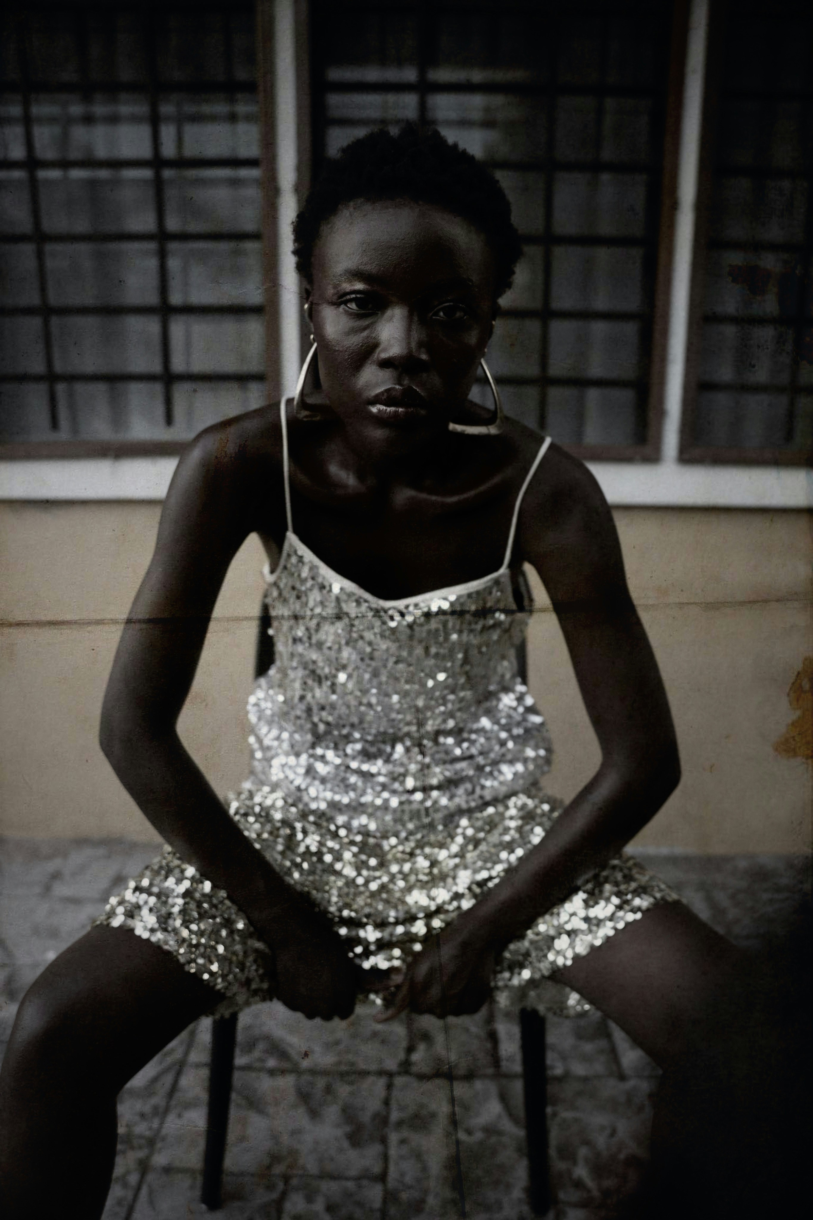 A woman in a sequined silver dress and large hoop earrings sitting on a chair