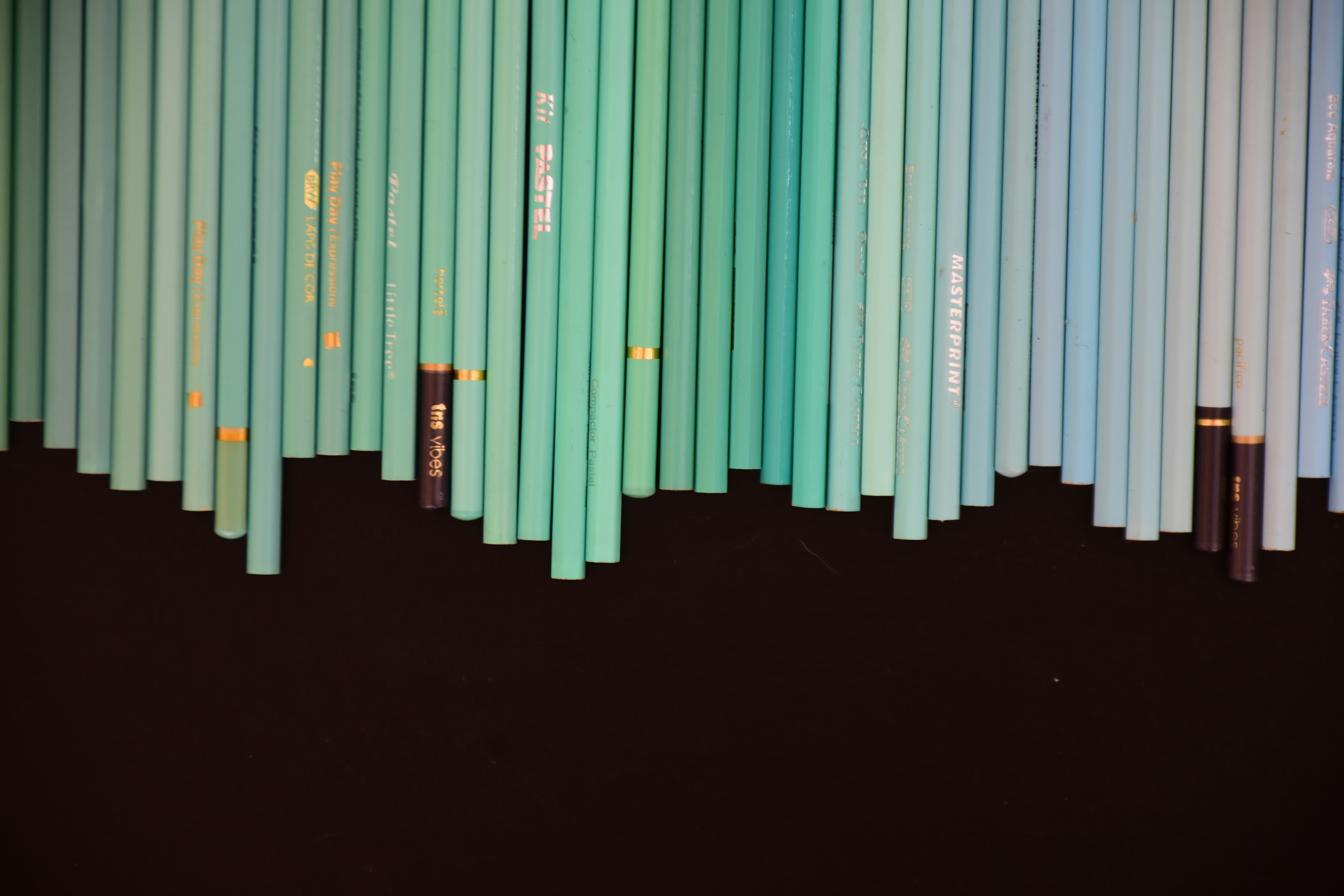 Une rangée de crayons bleu clair et turquoise disposés verticalement sur un fond noir