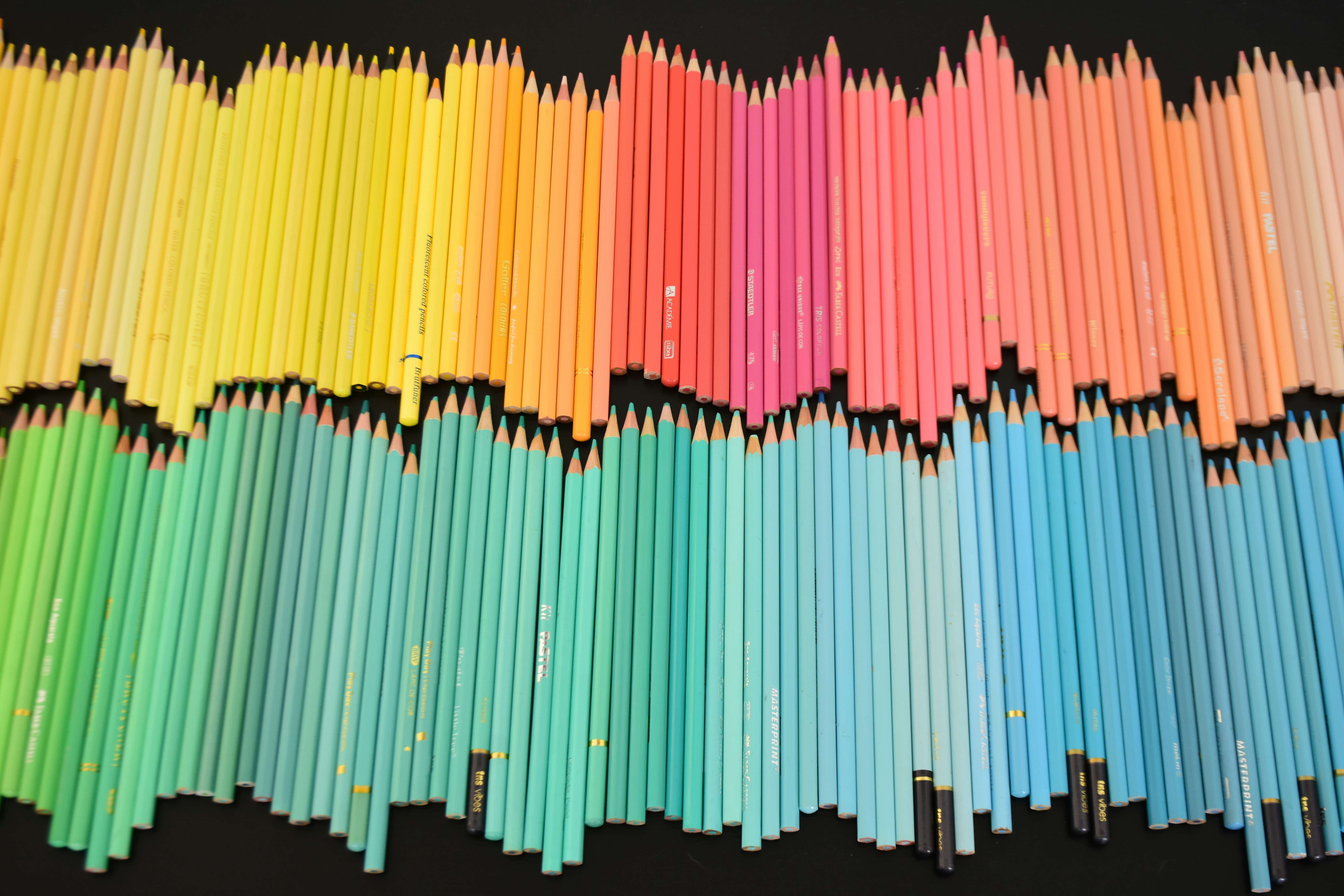 Une grande collection de crayons de couleur disposés en spectre sur un fond noir