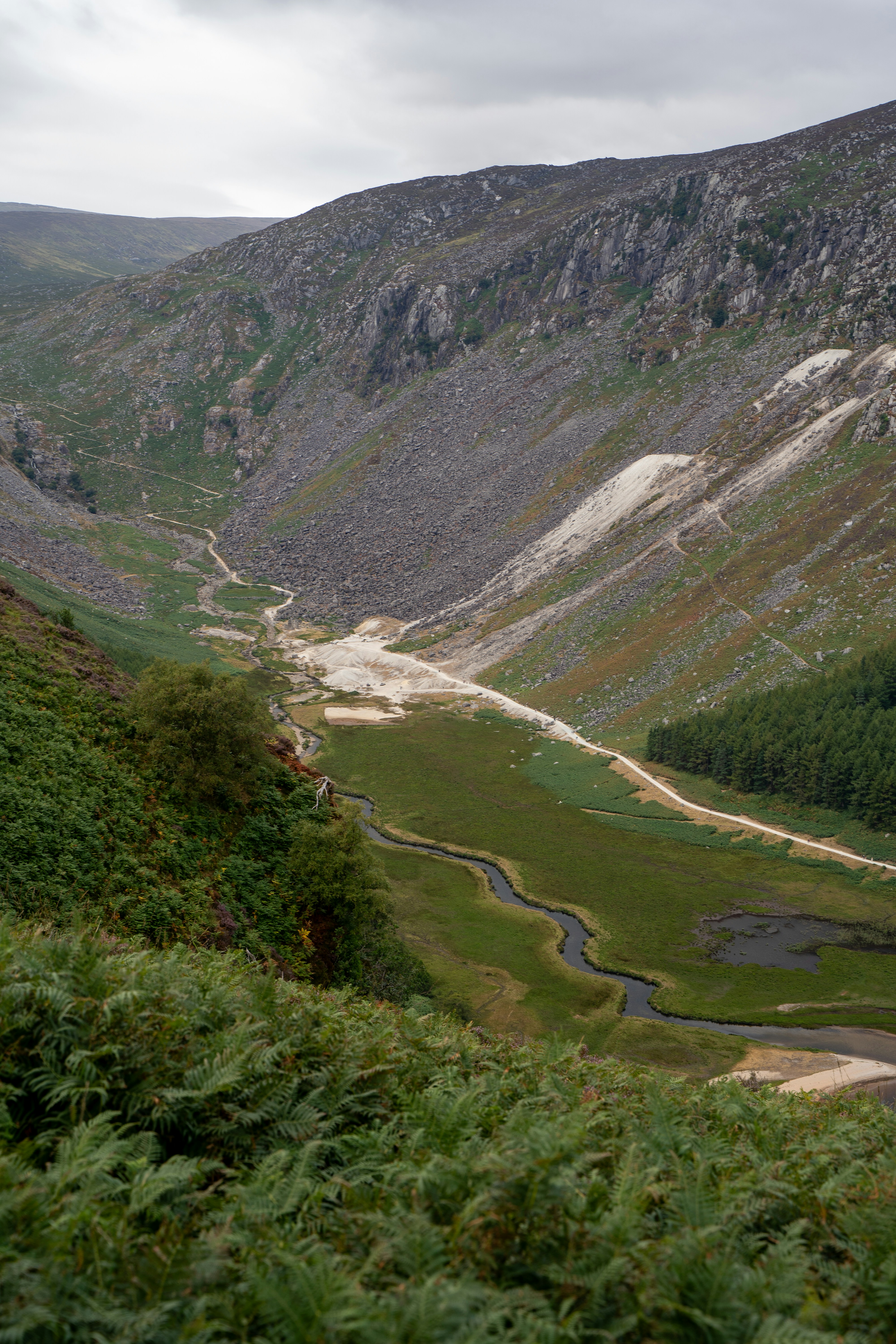 A winding stream through a green valley between steep rocky mountain slopes