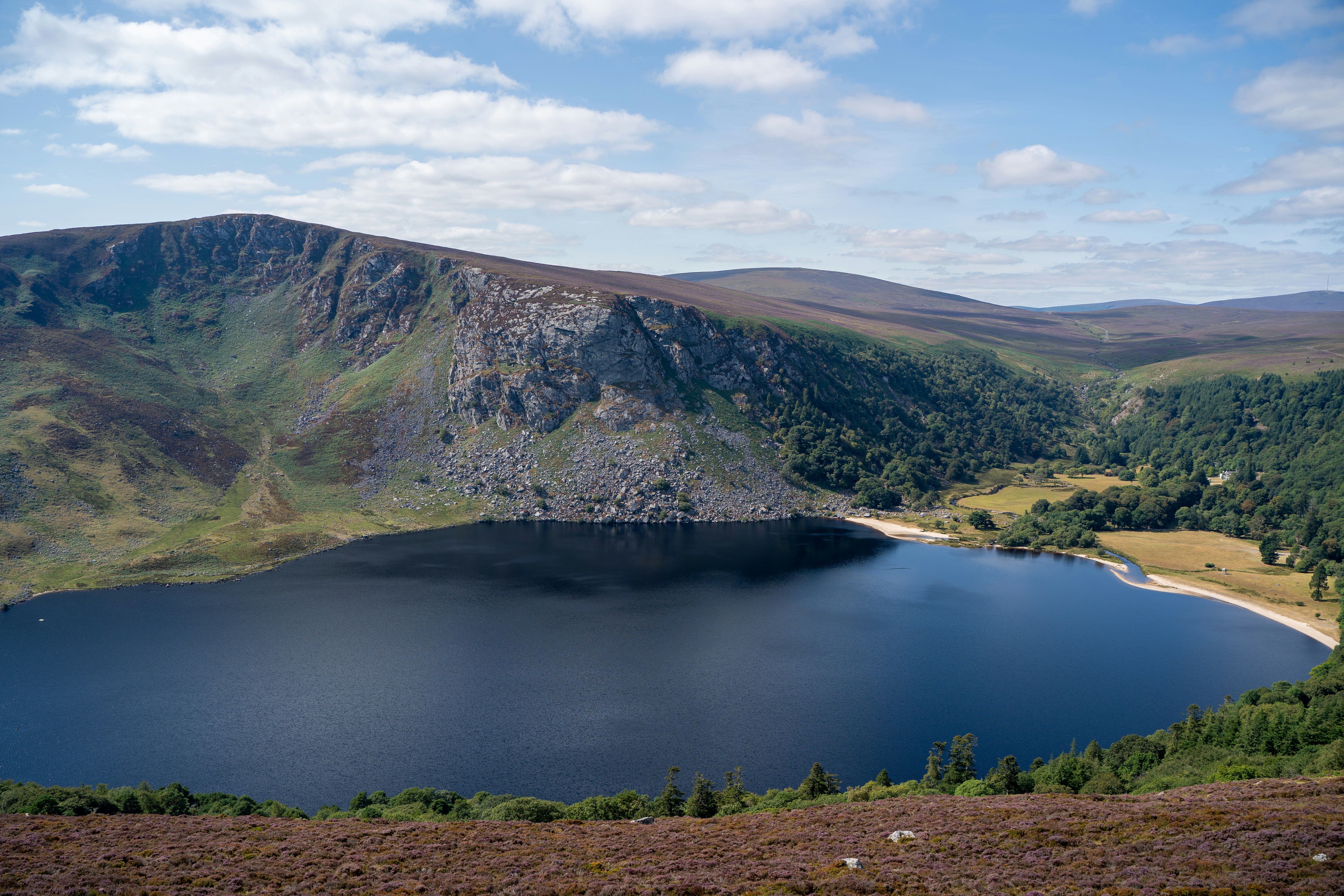 A dark lake nestled below a steep rocky mountain cliff in Glendalough