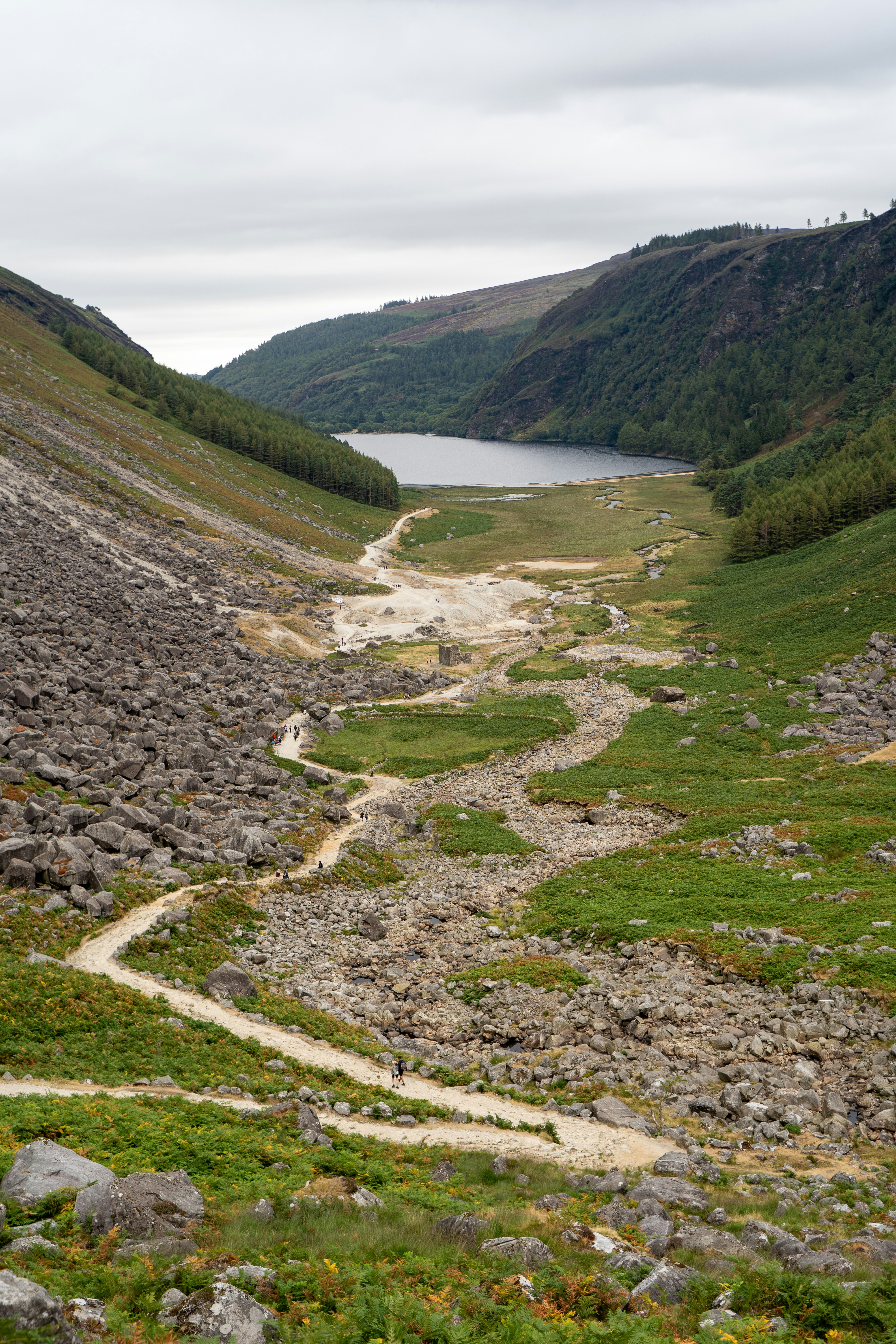 A winding dirt path through a rocky valley leading to a distant lake