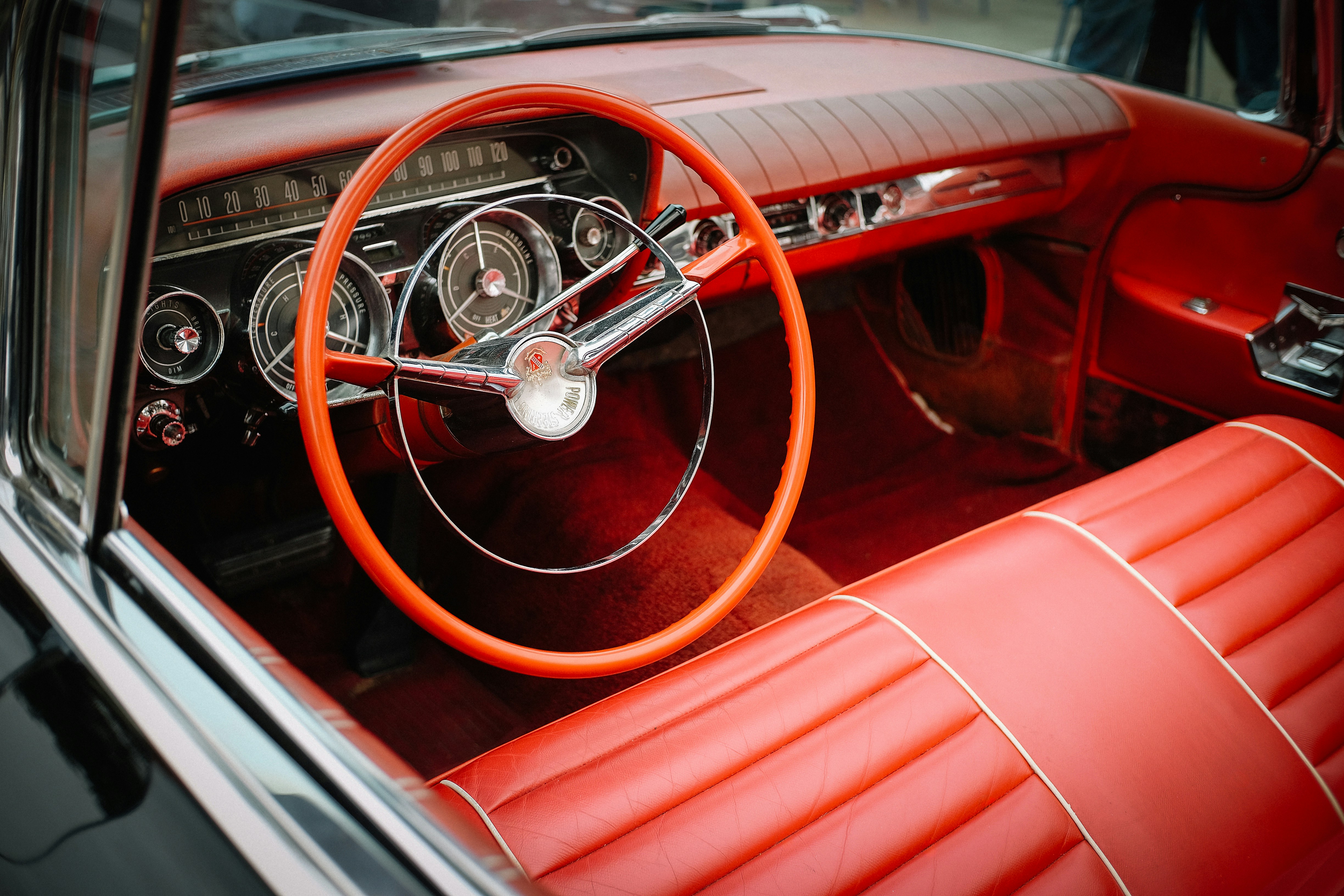 The interior of a vintage car with a bright orange steering wheel and red seats