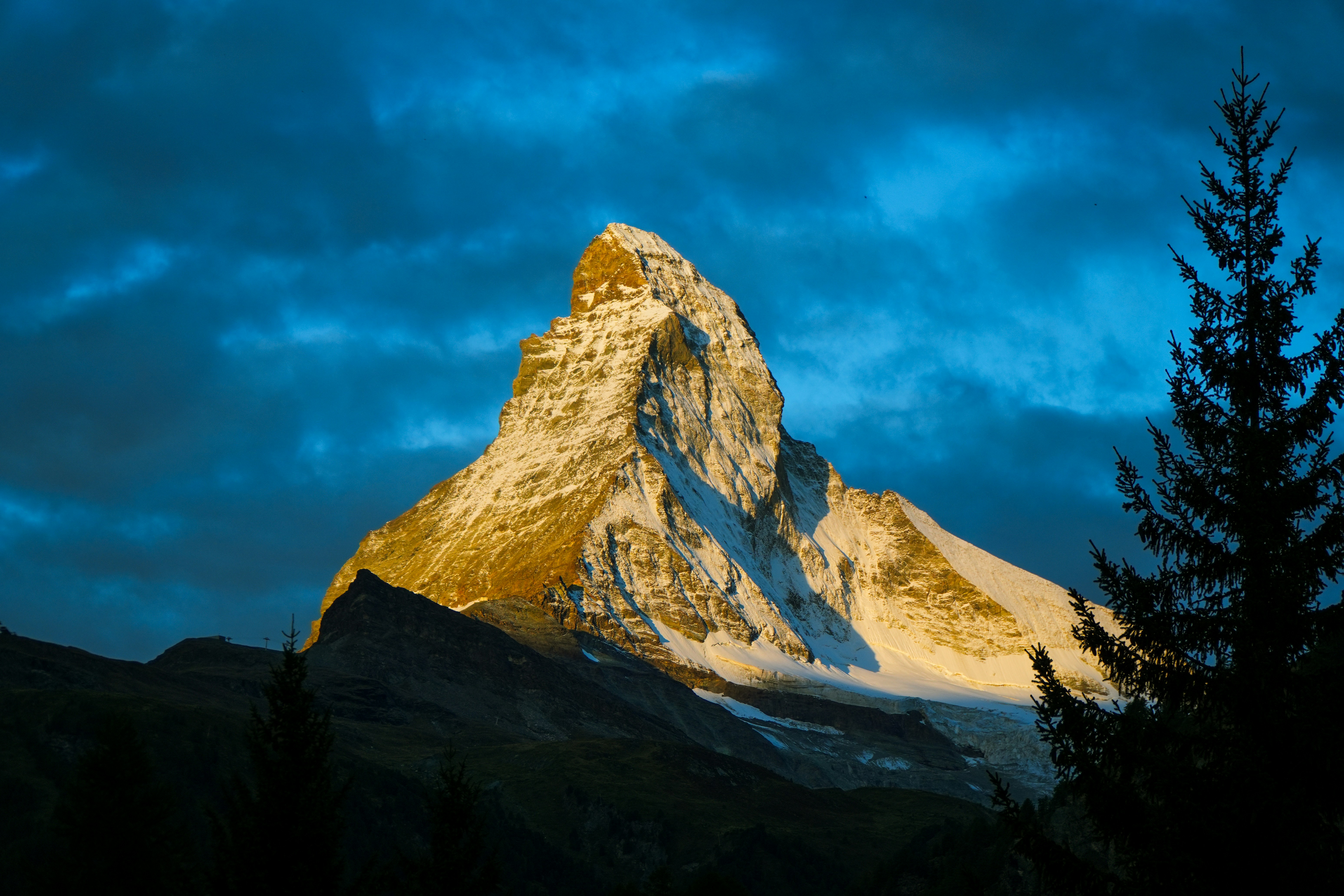 The Matterhorn peak illuminated by golden light against a deep blue cloudy sky