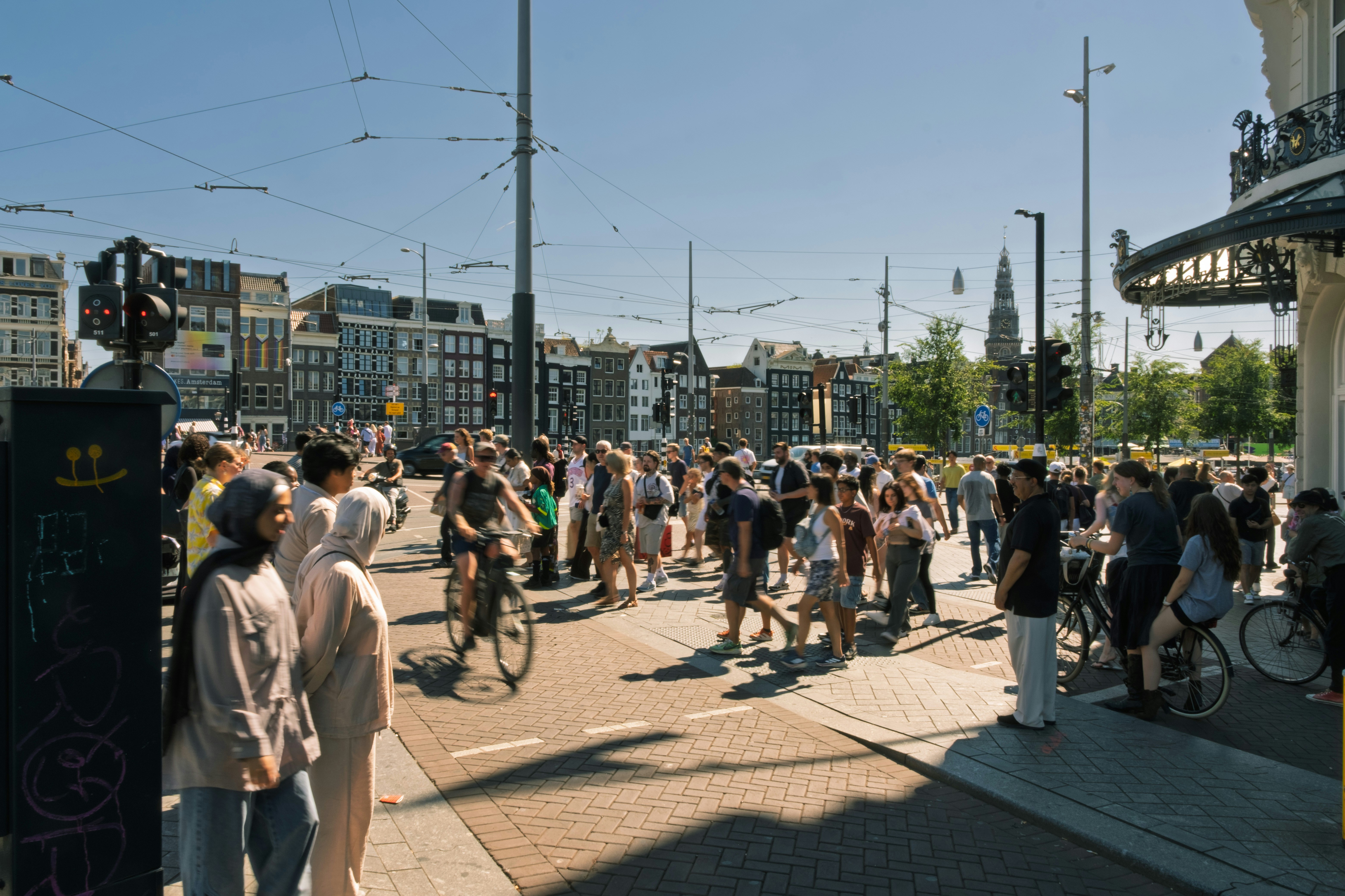 A crowd of people walking and cycling across a sunny intersection in Amsterdam