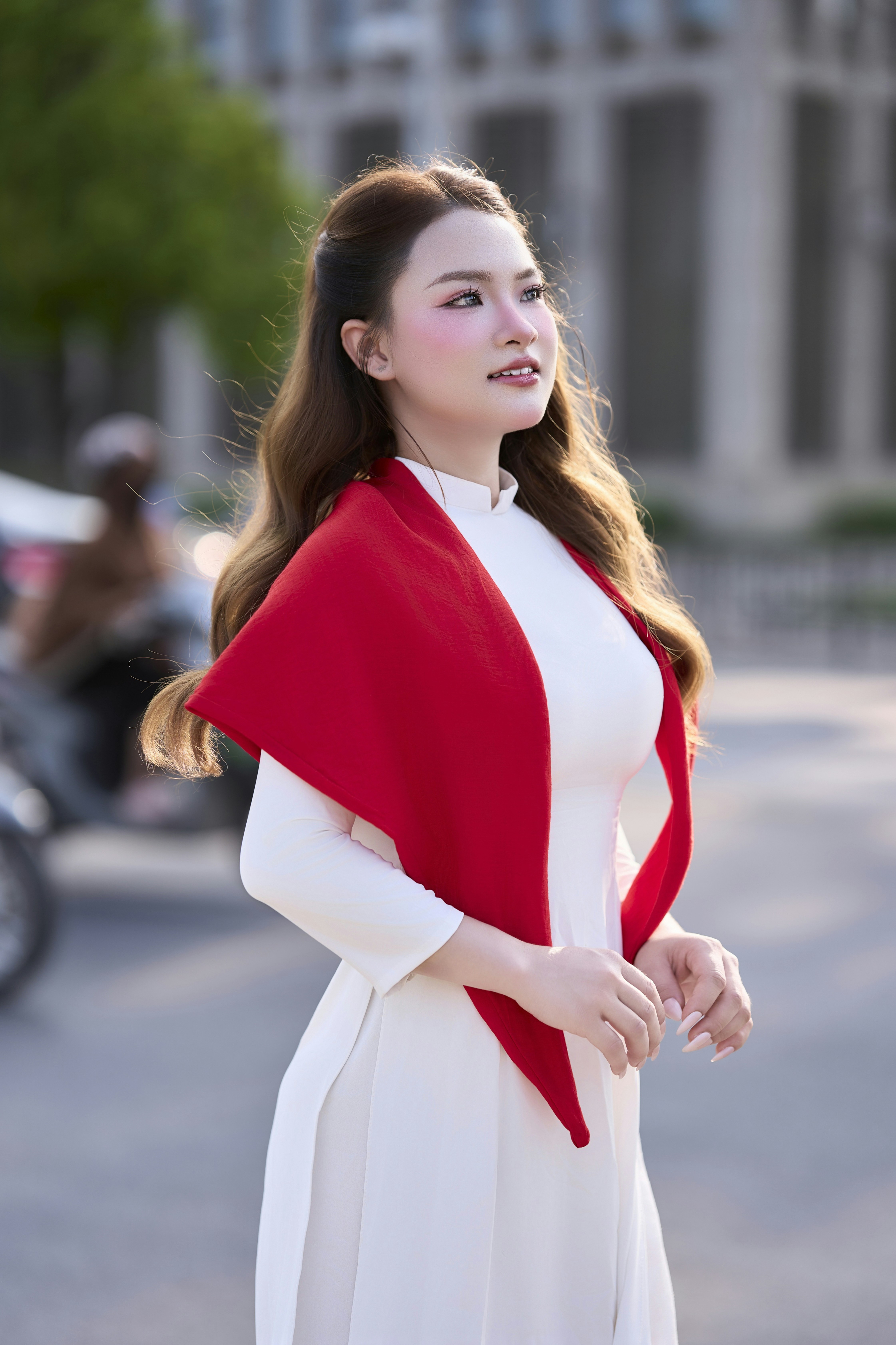 A woman in a white ao dai with a red scarf outdoors