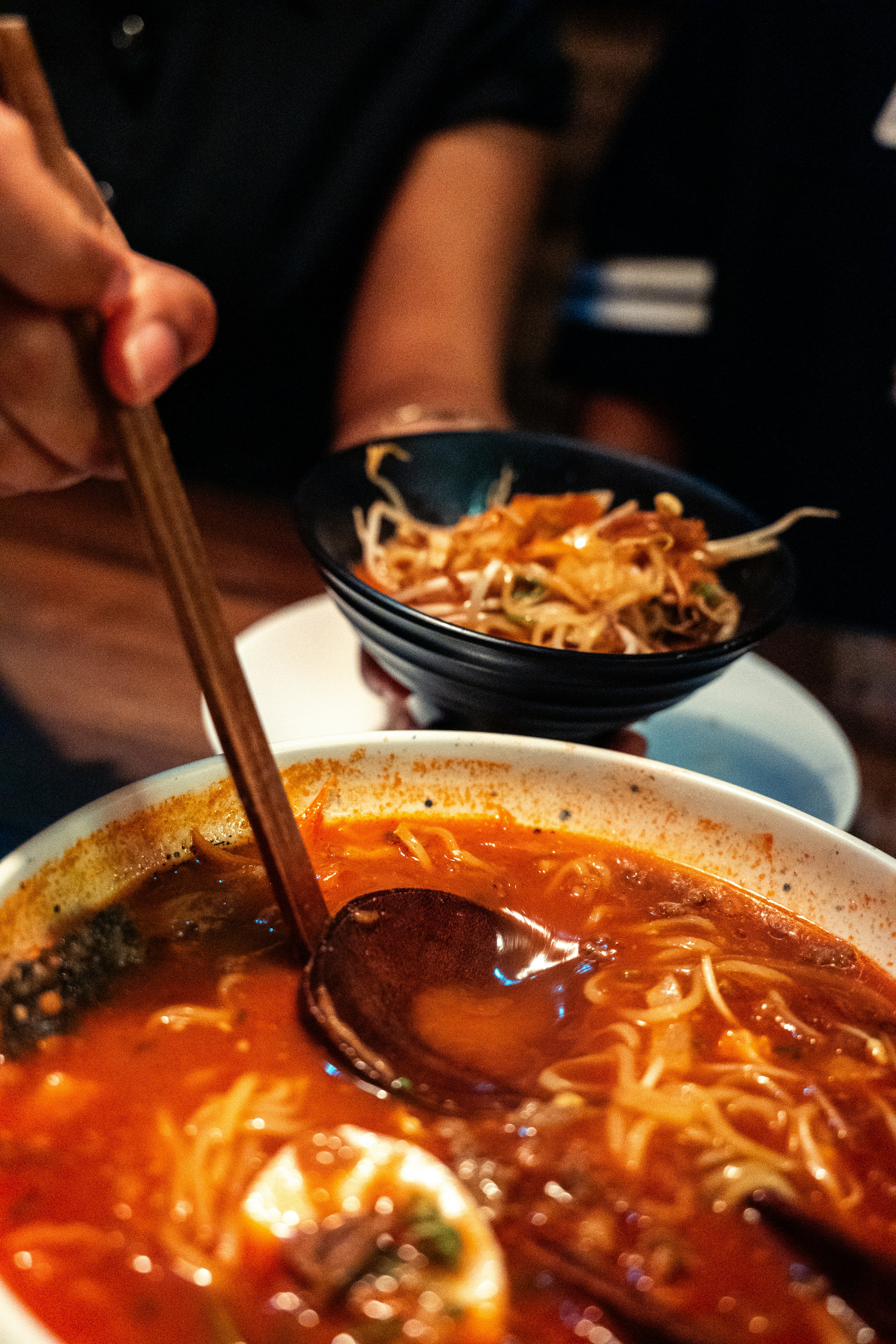 Una persona usando una cuchara de madera para remover ramen picante en un bol