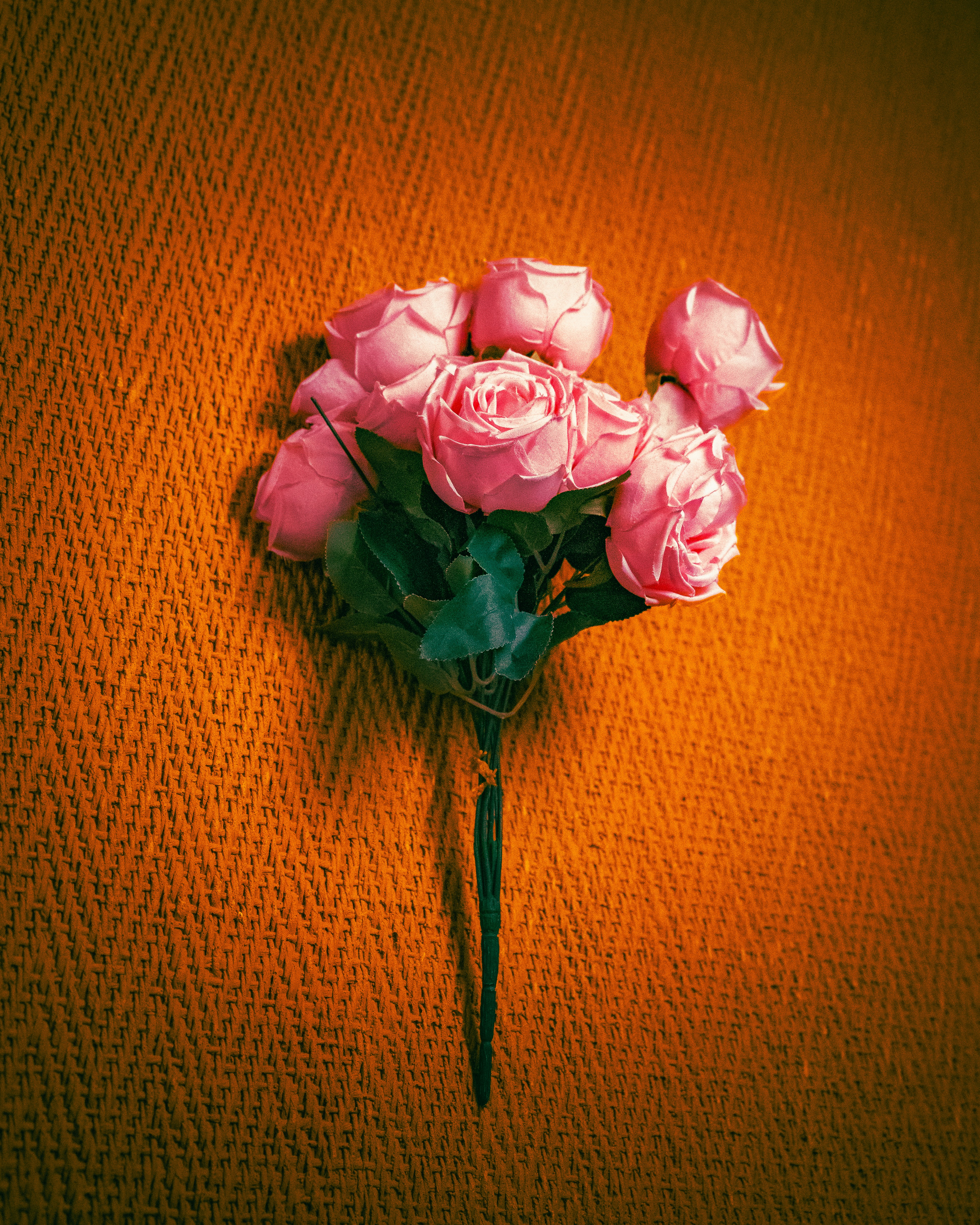 Un pequeño ramo de rosas artificiales rosas sobre una superficie naranja texturizada