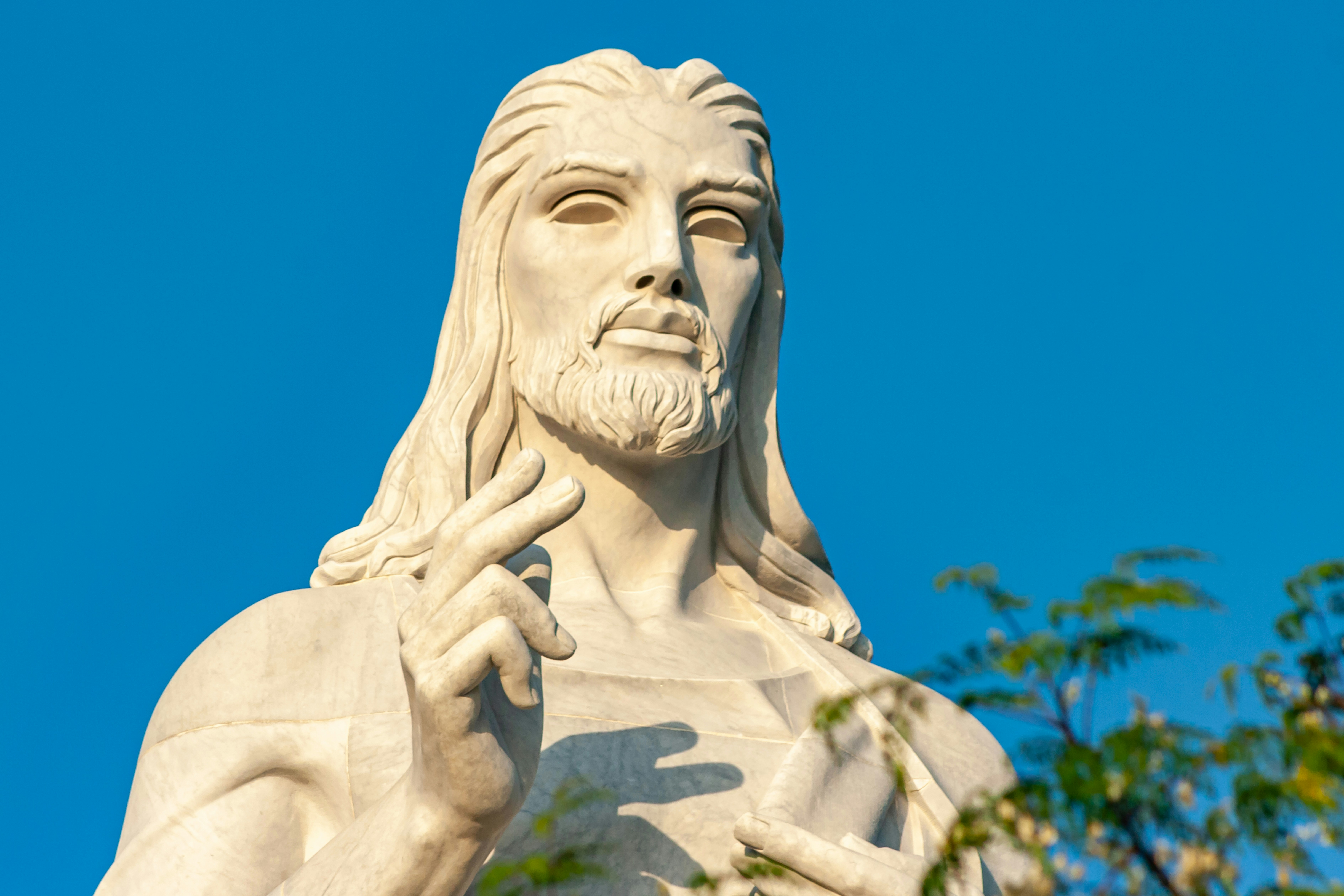 A white stone statue of a bearded man with long hair against blue sky