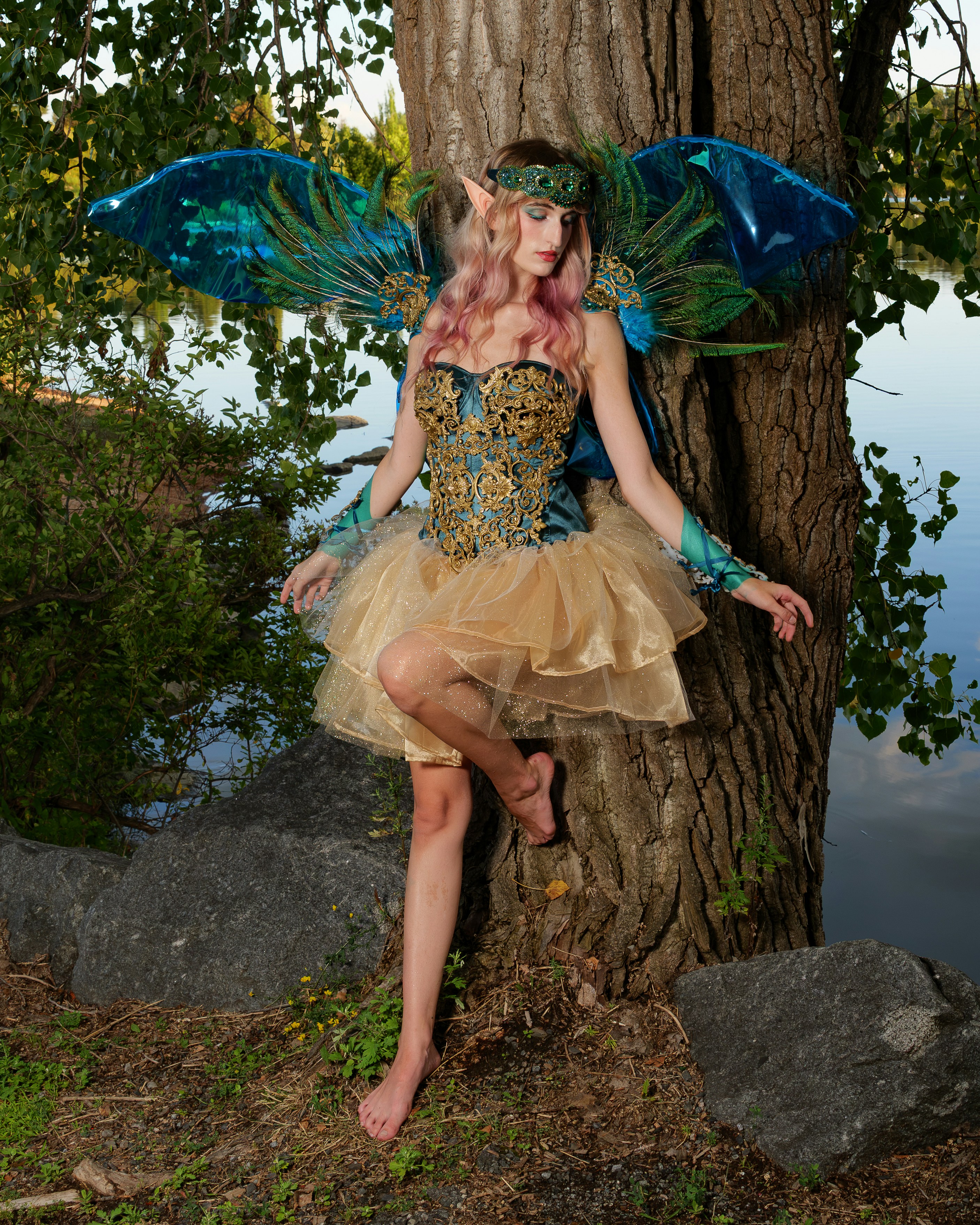 A person in a fairy costume with blue wings leaning against a tree