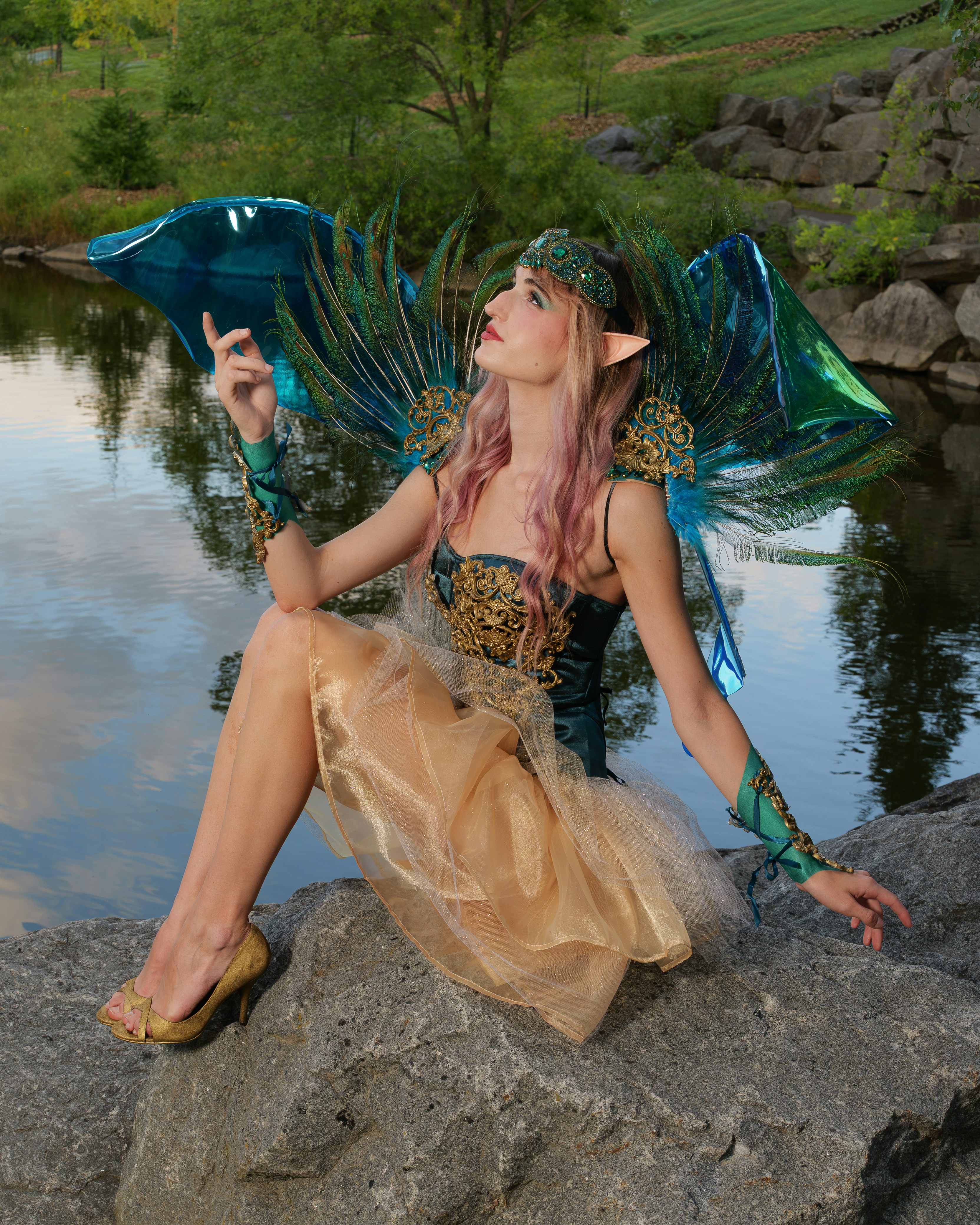 A person in a fairy costume with peacock feather wings on a rocky shore