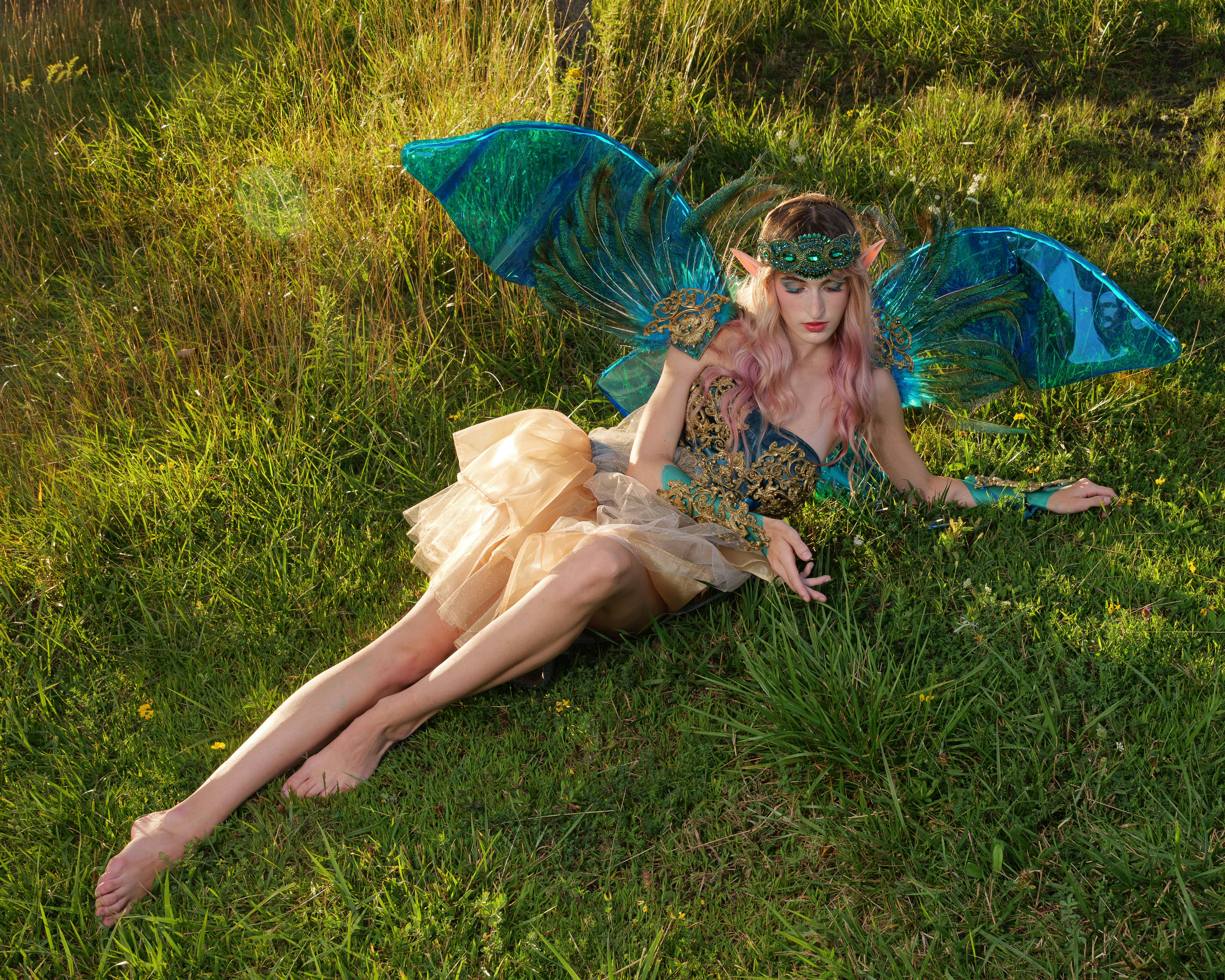 A person in a fairy costume with blue wings lying in tall green grass