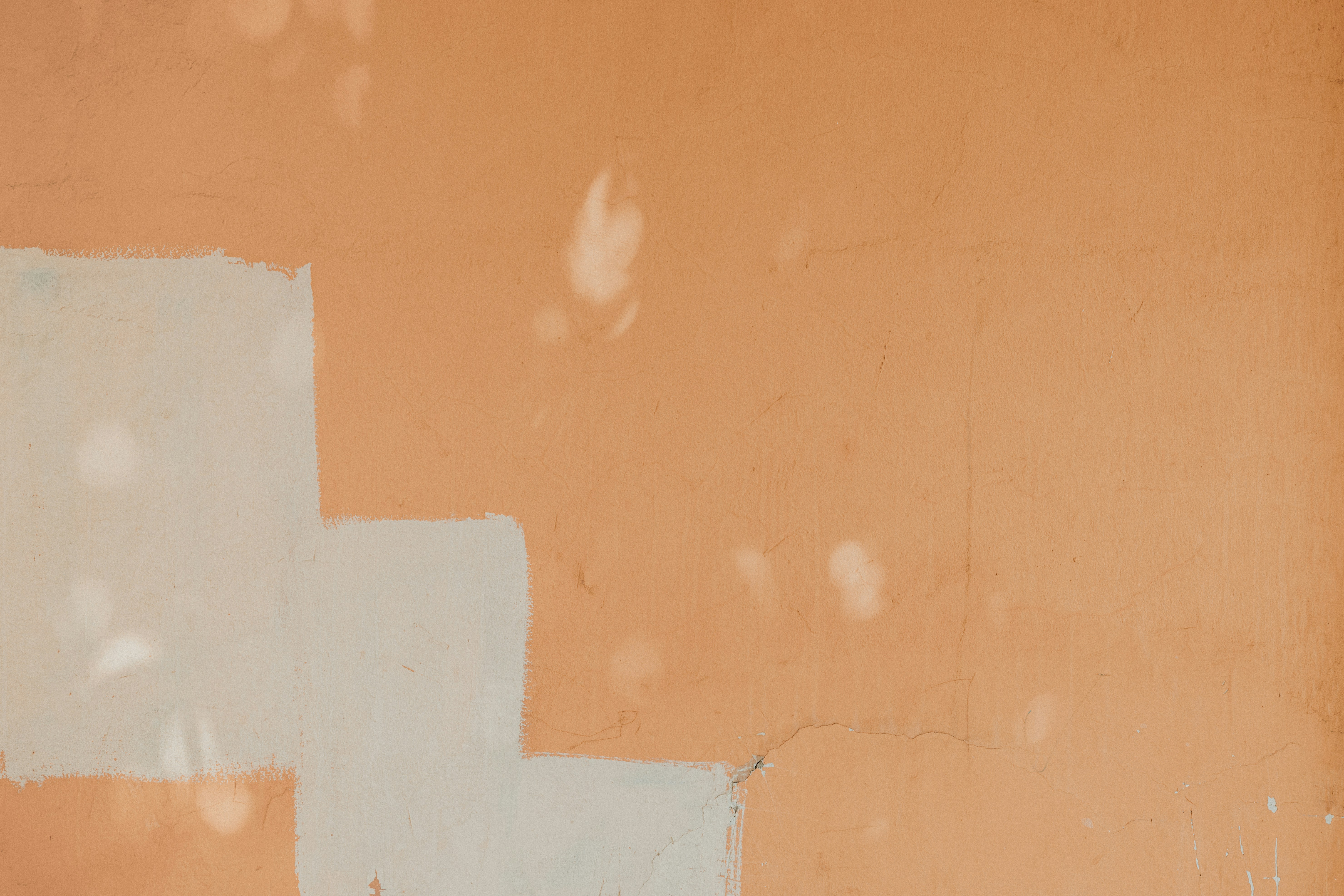 Una pared melocotón texturizada con una gran forma pintada de blanco y reflejos de luz