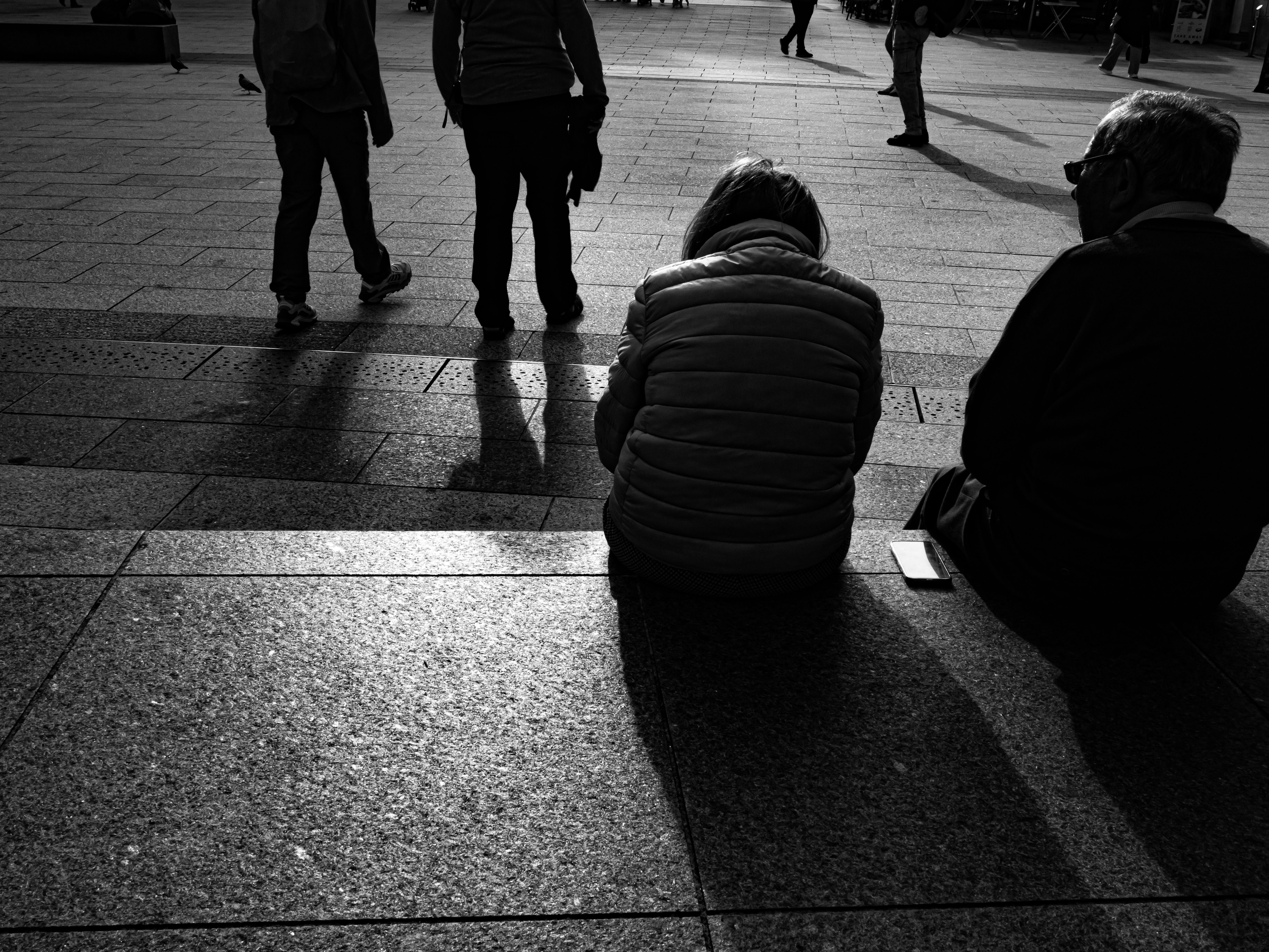 Two people sitting on stone steps with pedestrians walking in the background