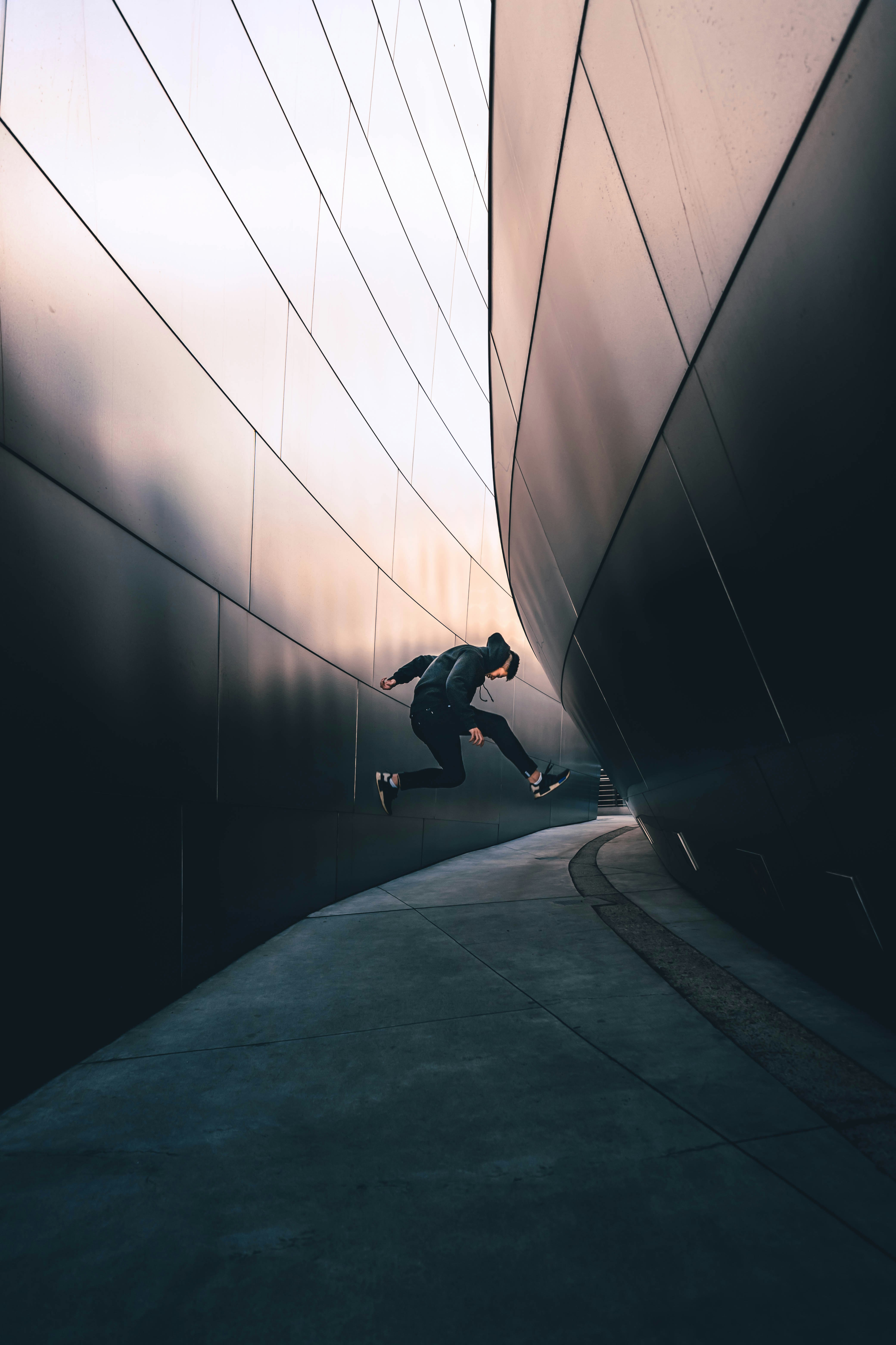 A person in a black hoodie jumping between two curved metallic walls