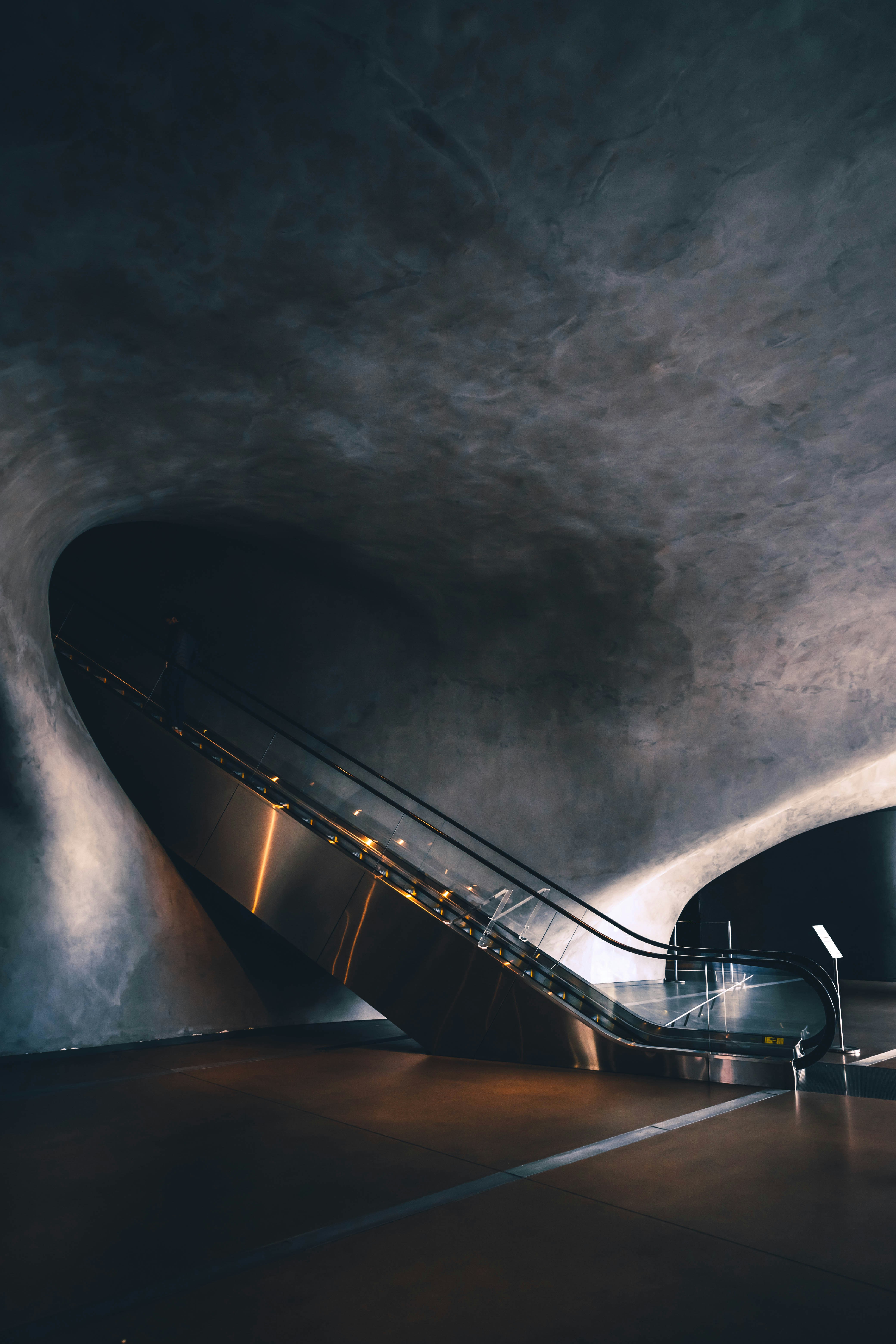 An escalator ascending into a dark cavernous space with smooth grey concrete walls
