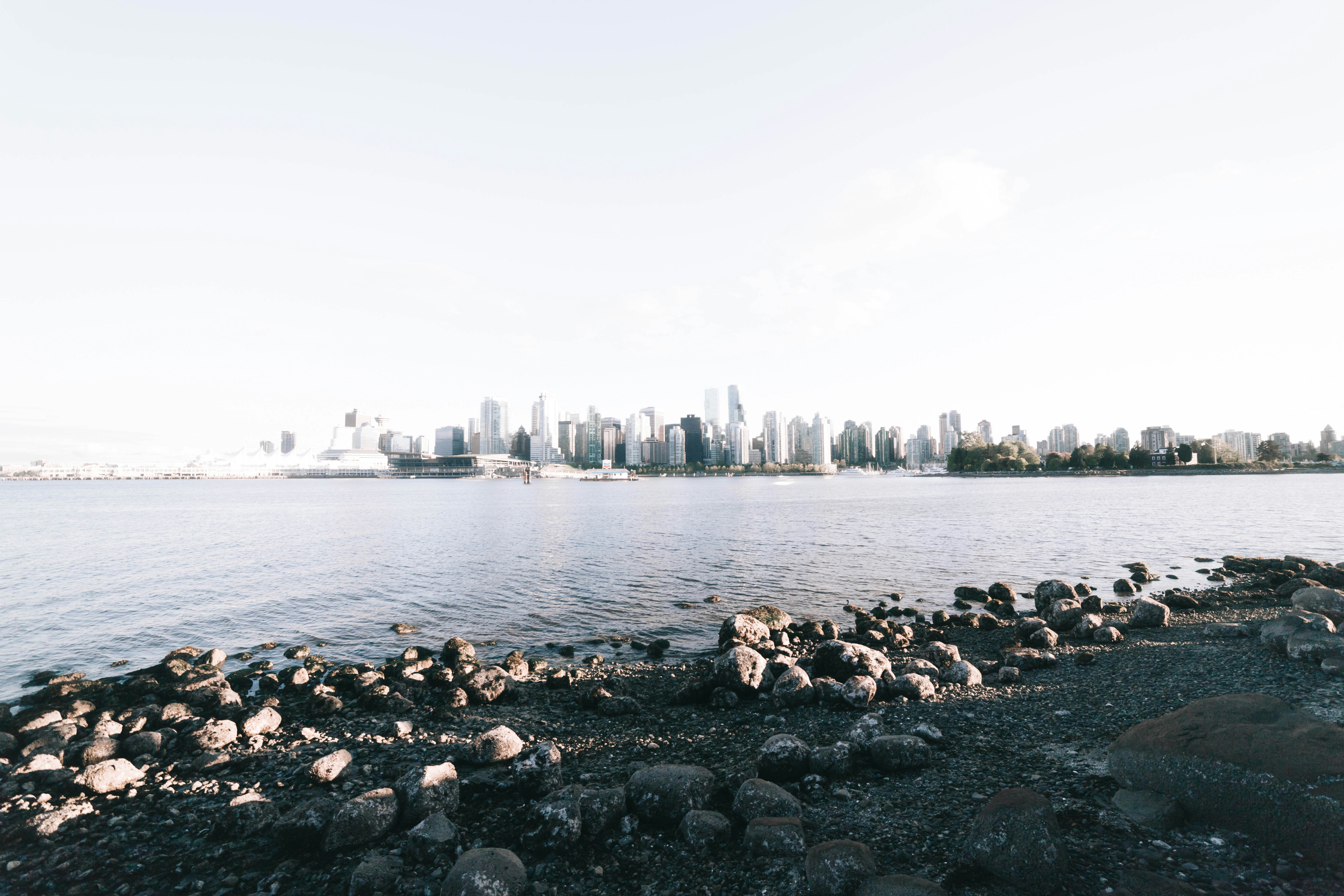 A rocky shoreline in the foreground looking across water toward a distant city skyline