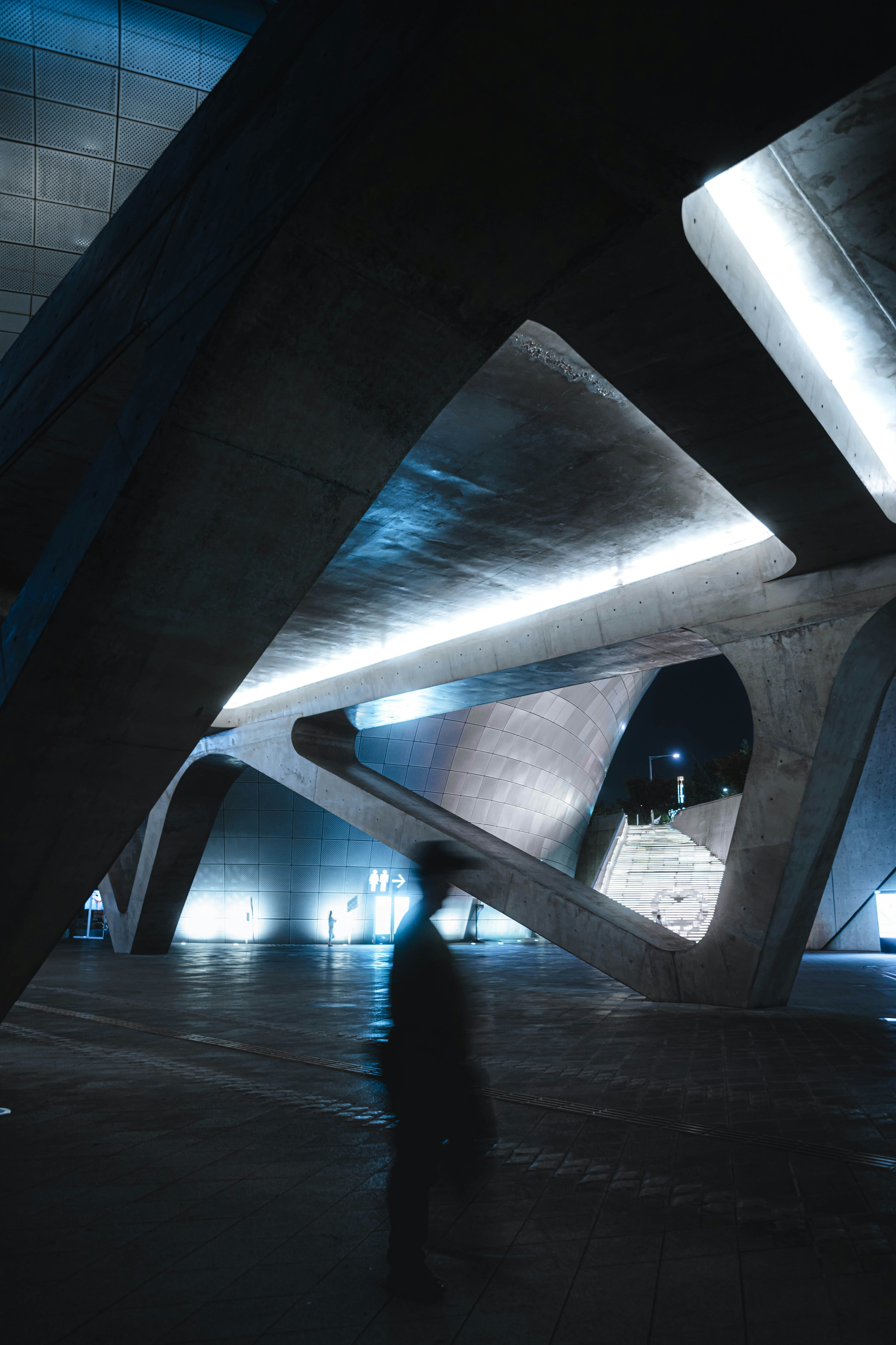 A blurred person walking through a modern concrete structure with illuminated stairs at night