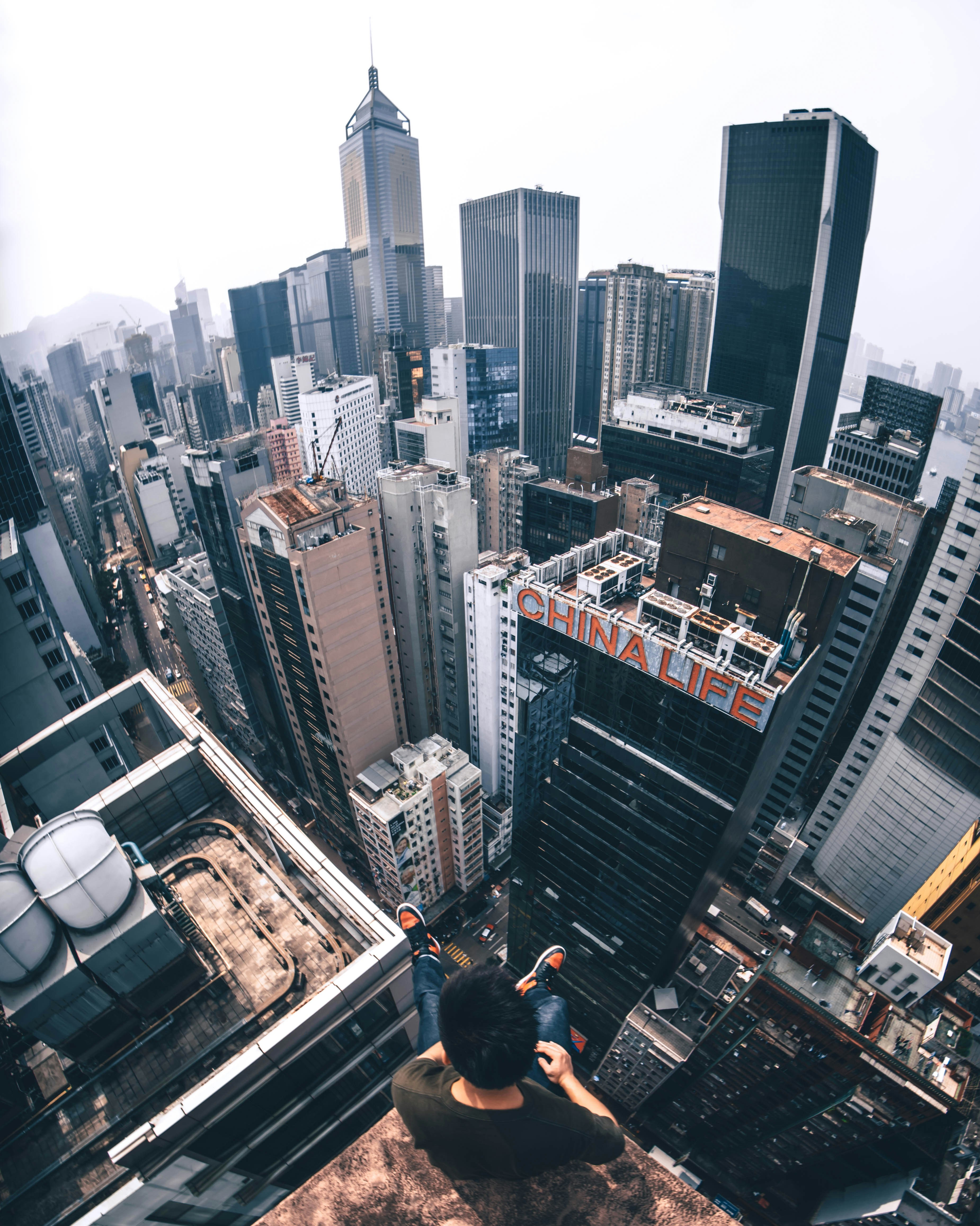 A person sitting on a skyscraper edge overlooking a dense city skyline