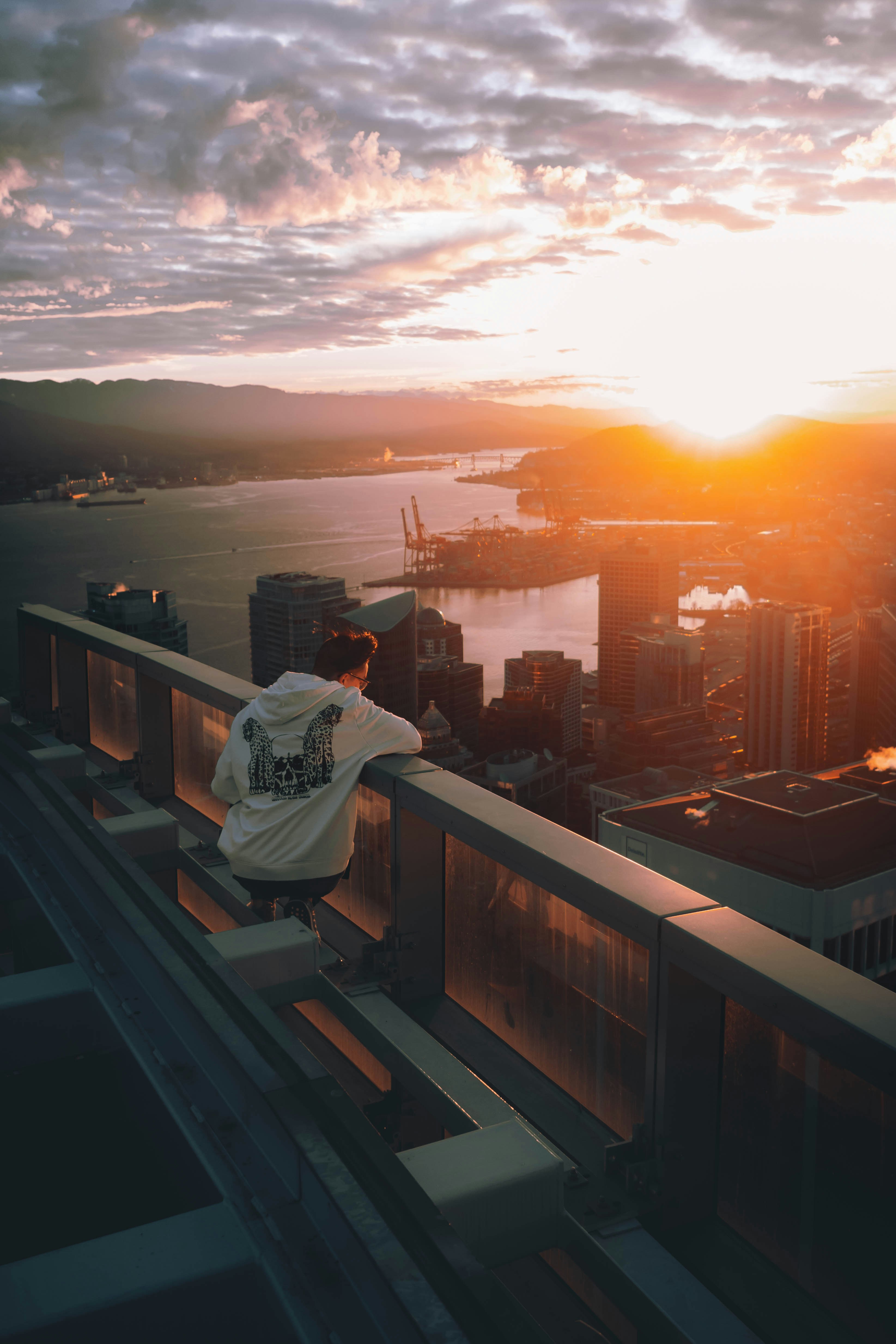 A person in a white hoodie leaning on a glass railing overlooking Vancouver