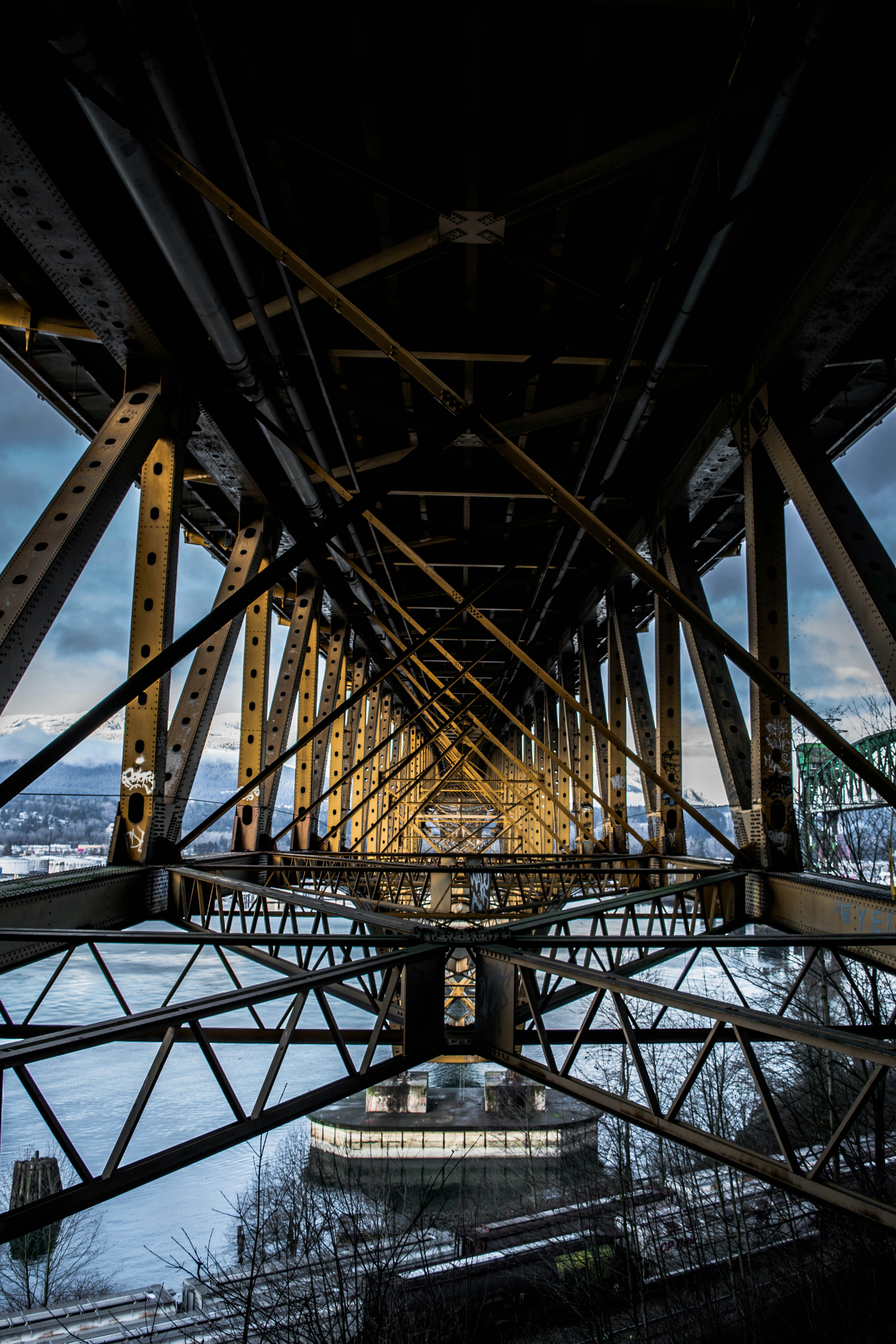 The yellow steel truss structure of a bridge spanning a wide river