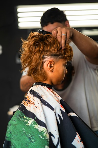 Barber styling curly hair with a shaved-in design