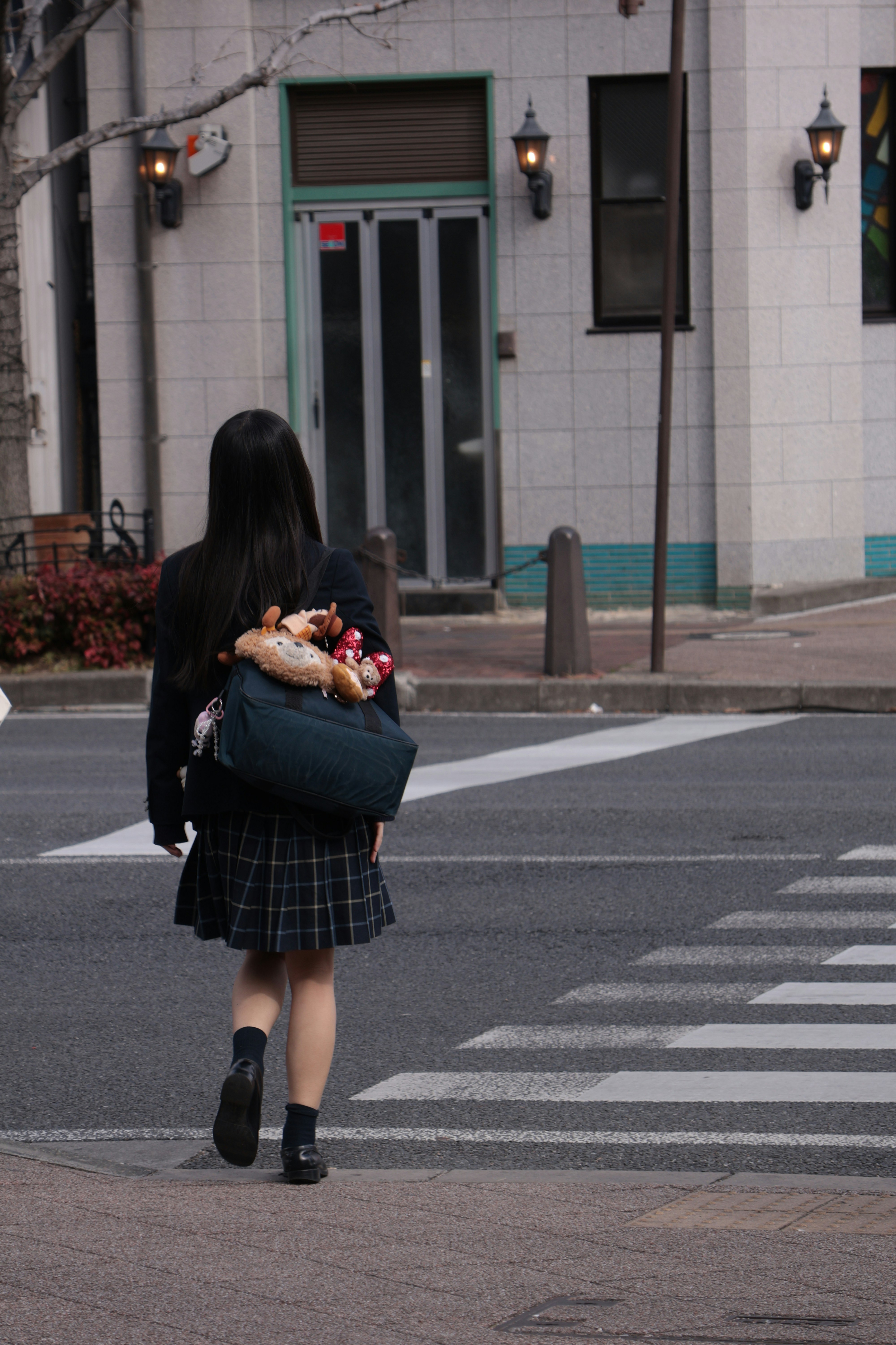 A student with a plush-covered bag walking across a city crosswalk