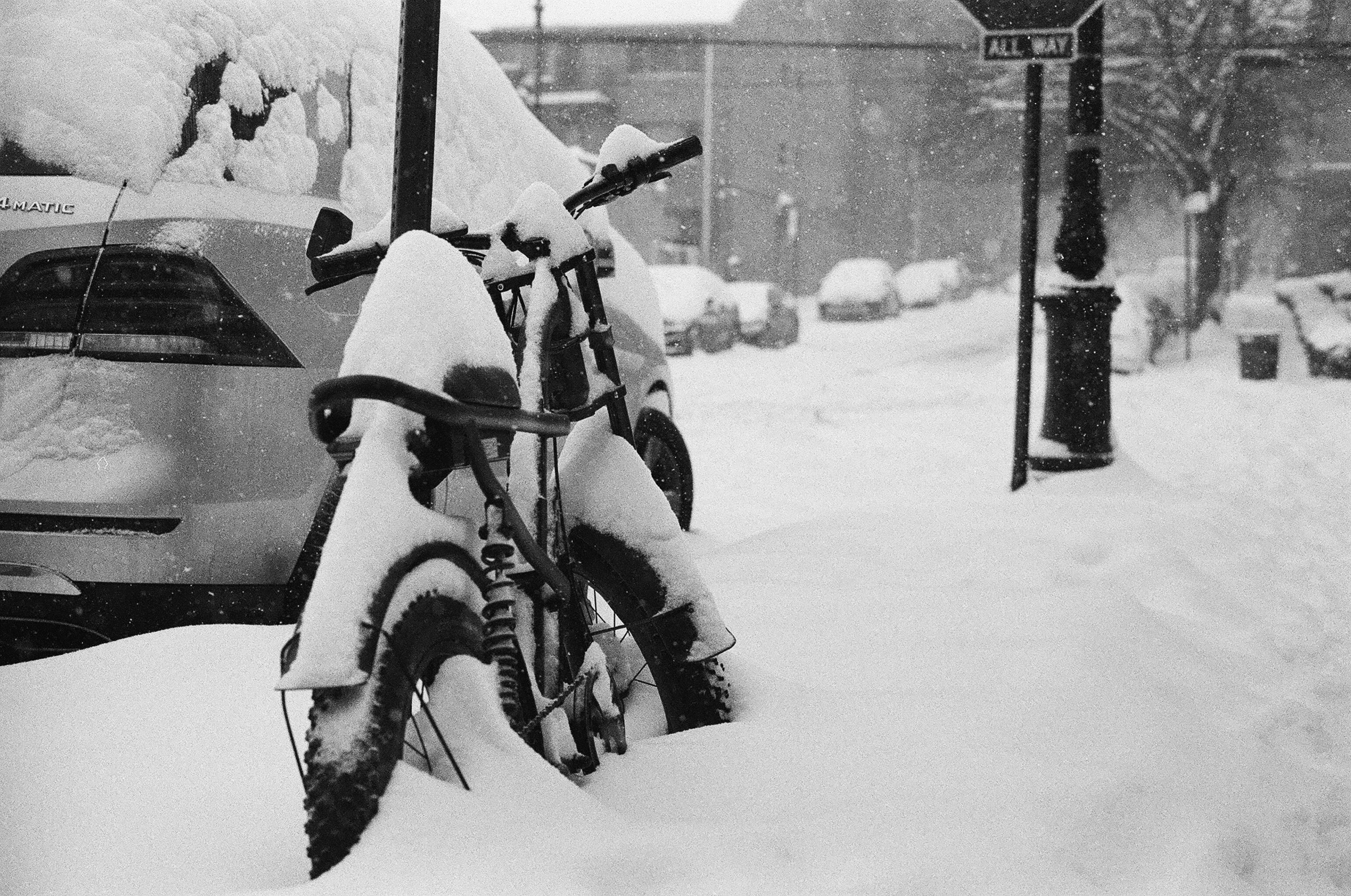 A bicycle covered in deep snow parked beside a car on a city street