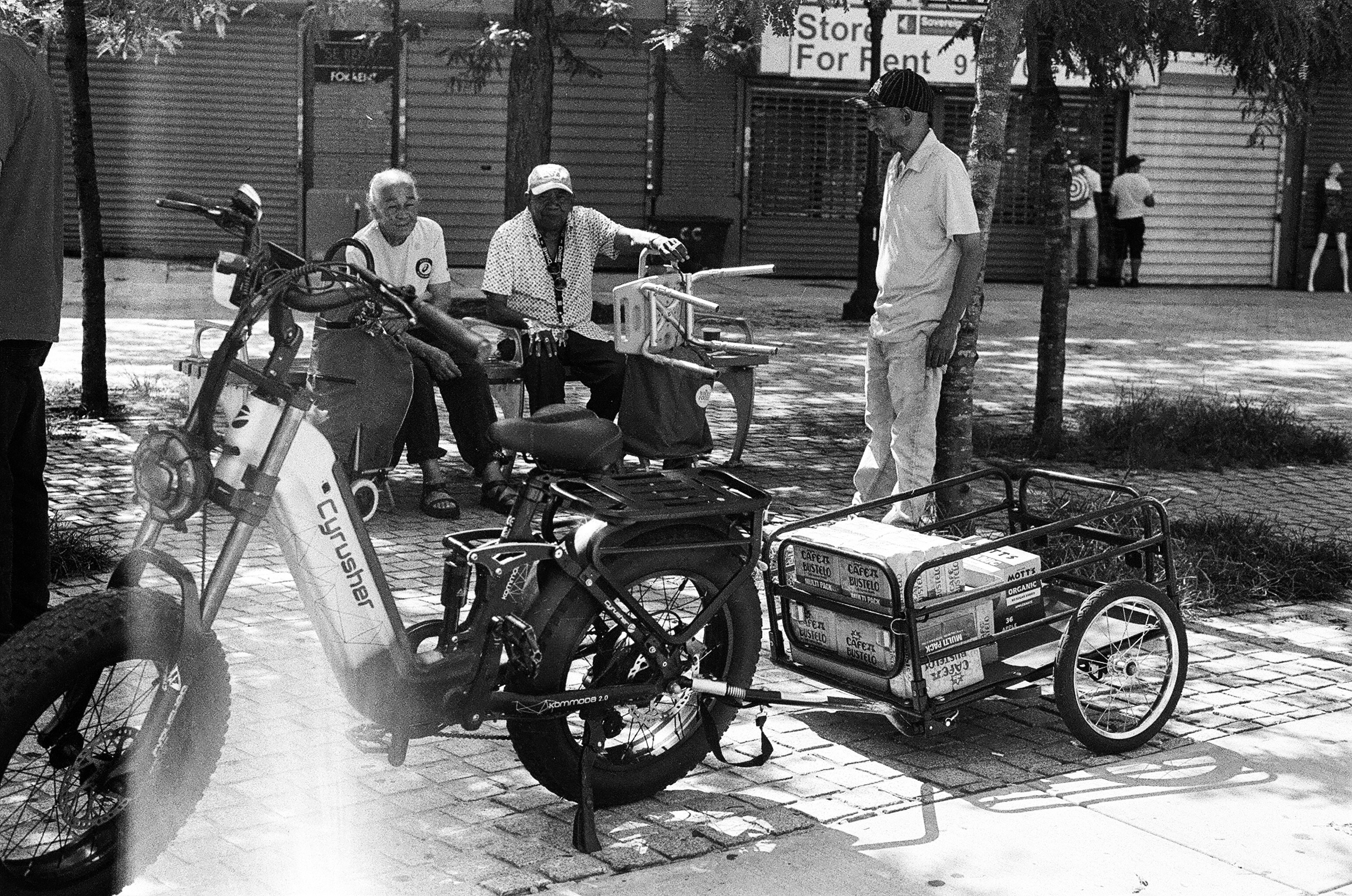 Three men on a sidewalk with an electric bike pulling a cargo trailer