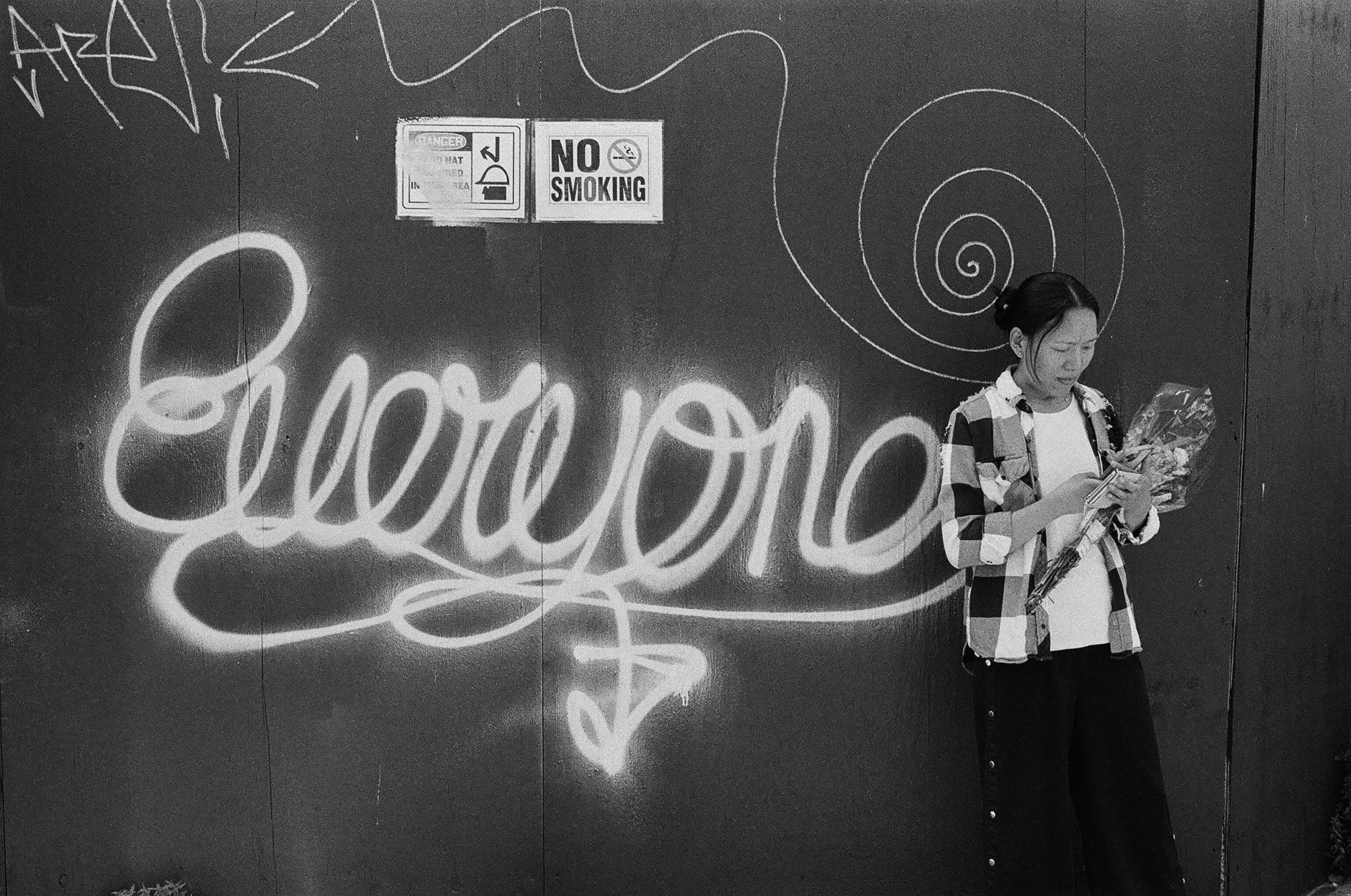 A person in a plaid shirt holding flowers against a wall with graffiti